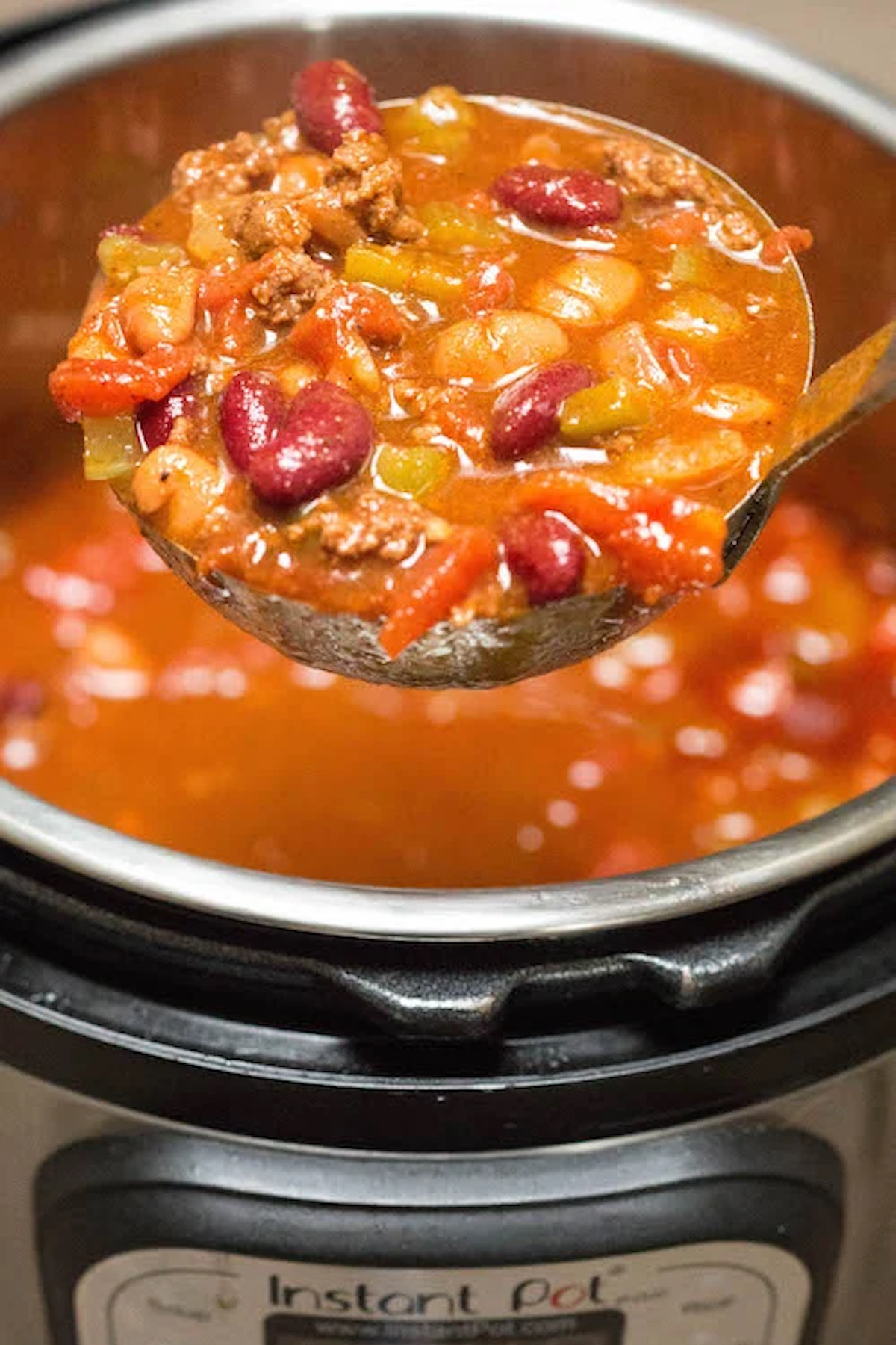 A ladle full of copycat Wendy's Chili is in focus over the Instant Pot which is out of focus.