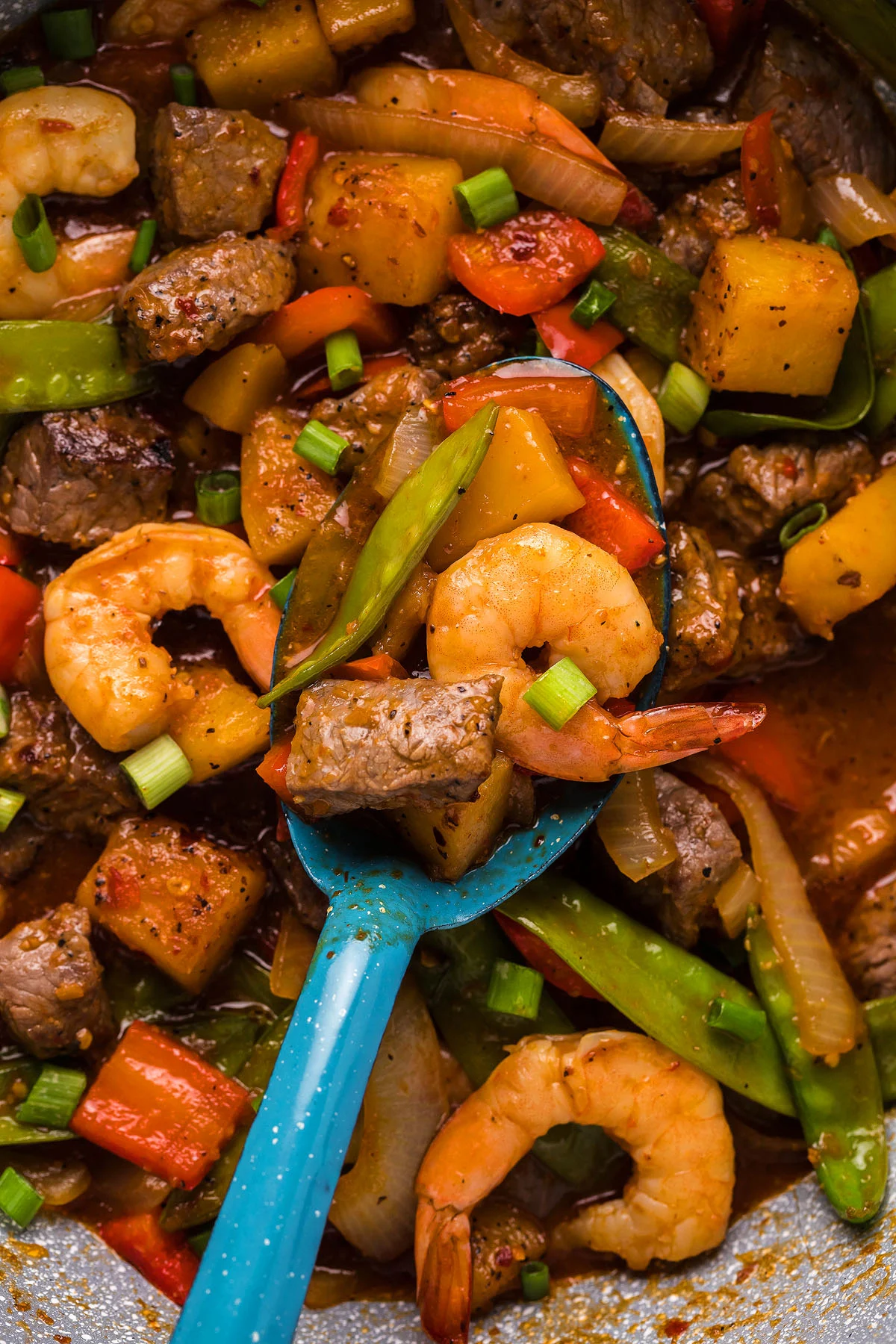 A skillet filled with steak bites, shrimp, snap peas, and bell pepper.