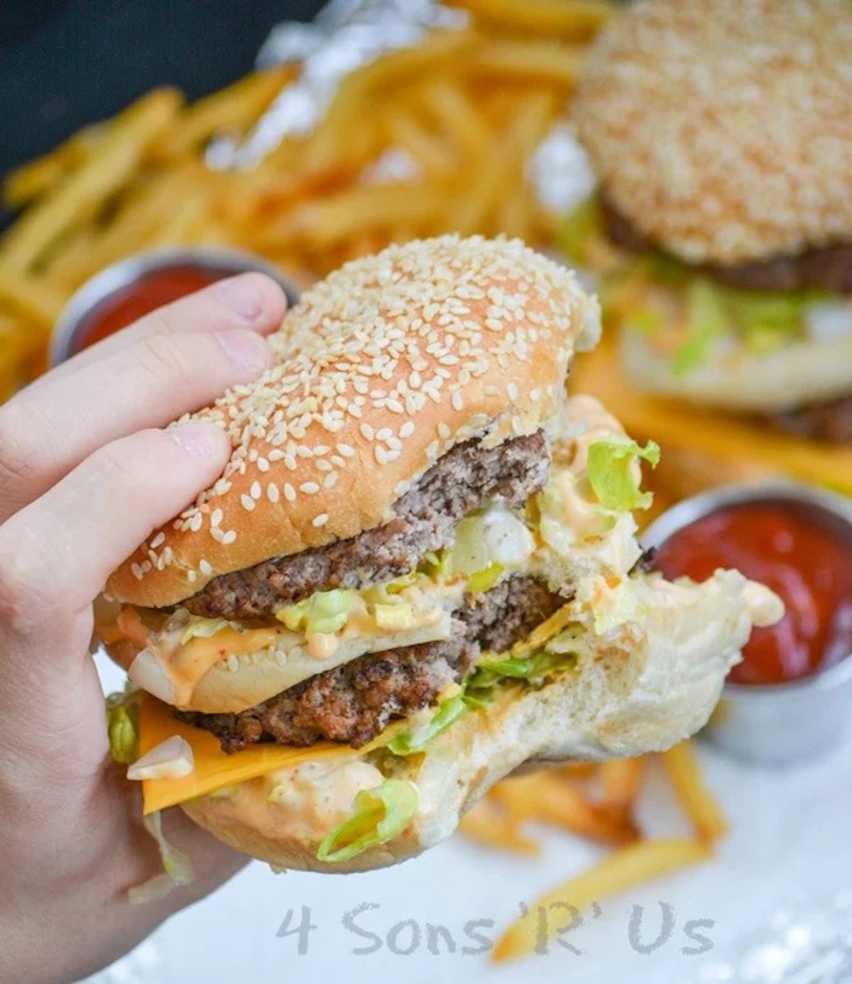 A hand holds up a homemade big mac that has a bite taken out of it.