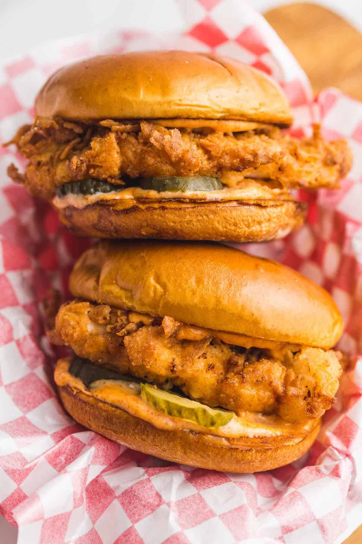 A food basket filled with homemade spicy chicken sandwiches with spicy mayo and pickles.