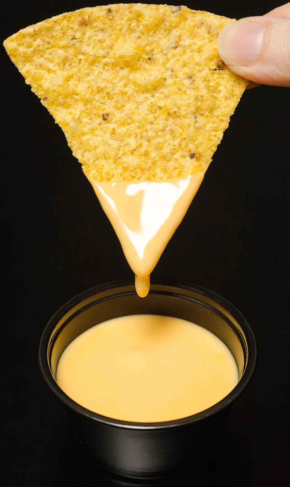 A hand holds a single tortilla chip that's been dipped in nacho cheese sauce.