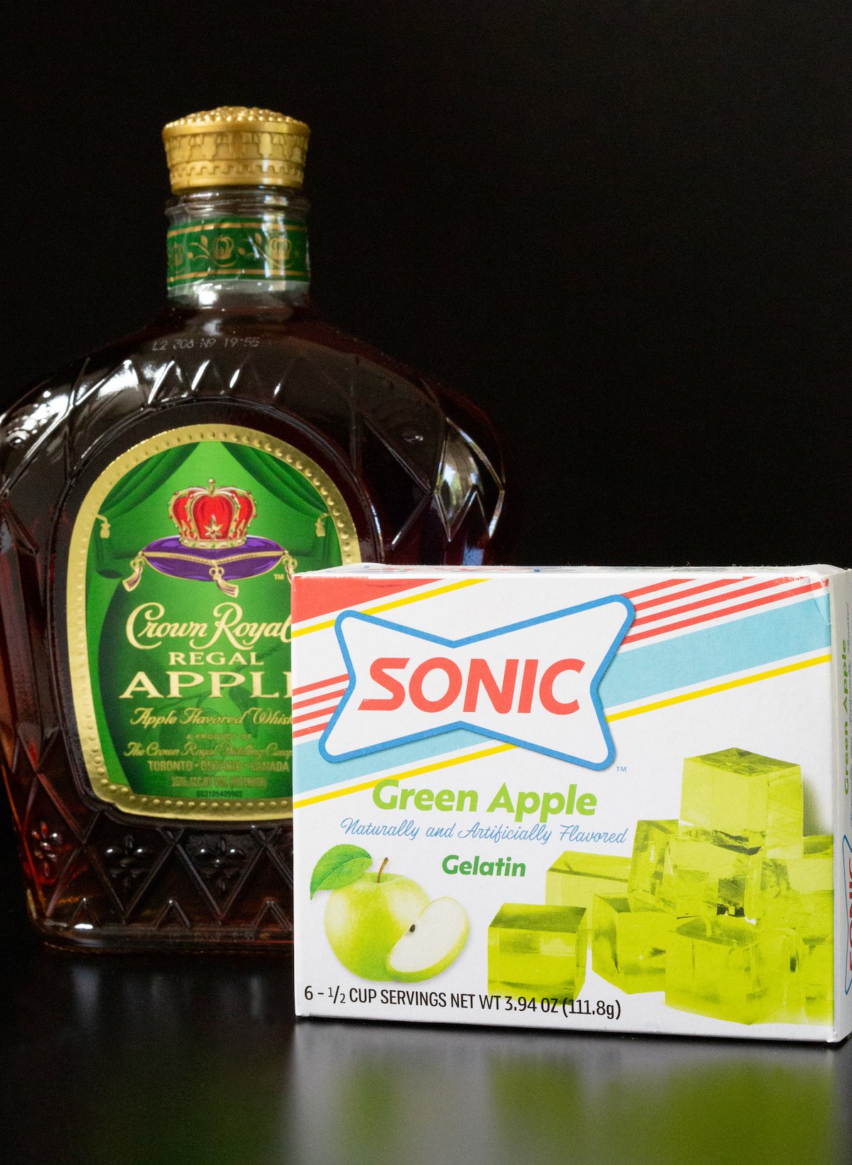A bottle of Crown Apple whisky and a box of Sonic green apple gelatin on a black background.