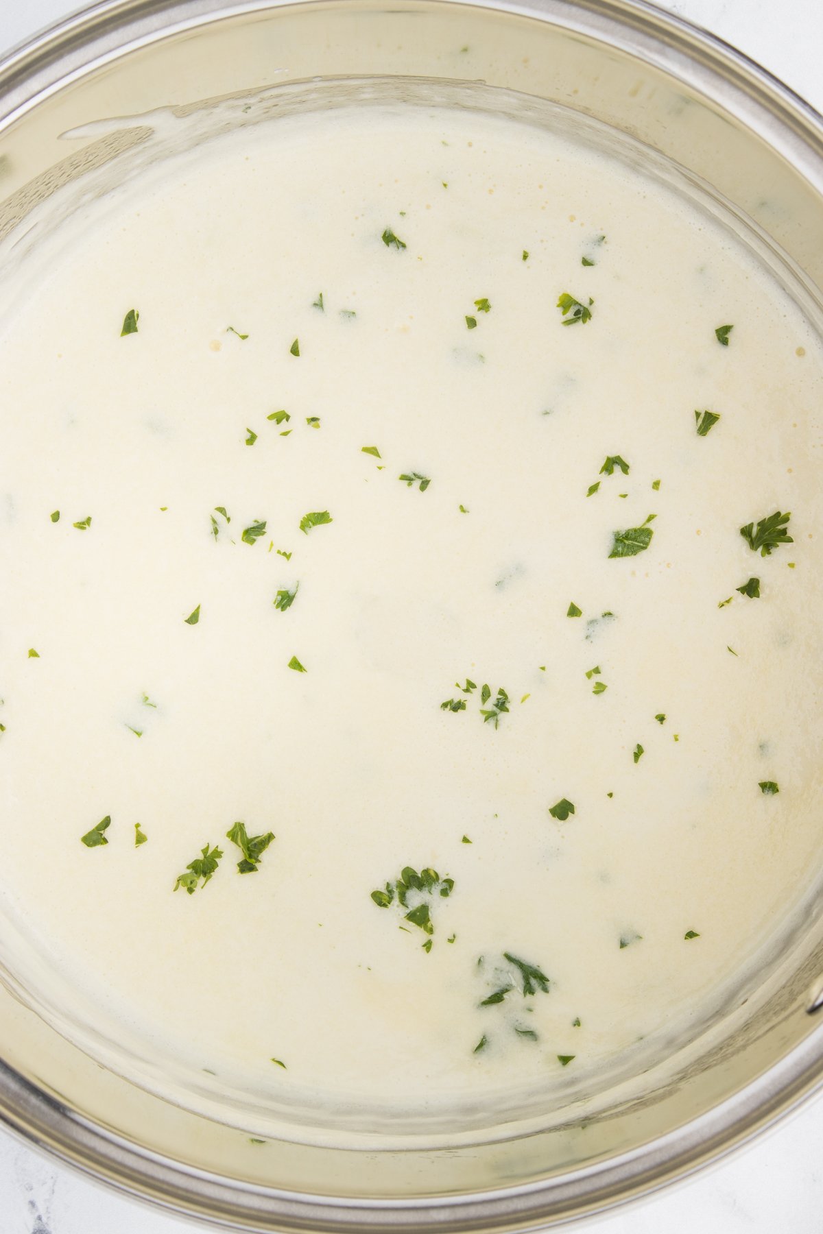 A small metal bowl with white garlic cream sauce that's garnished with fresh chopped parsley.