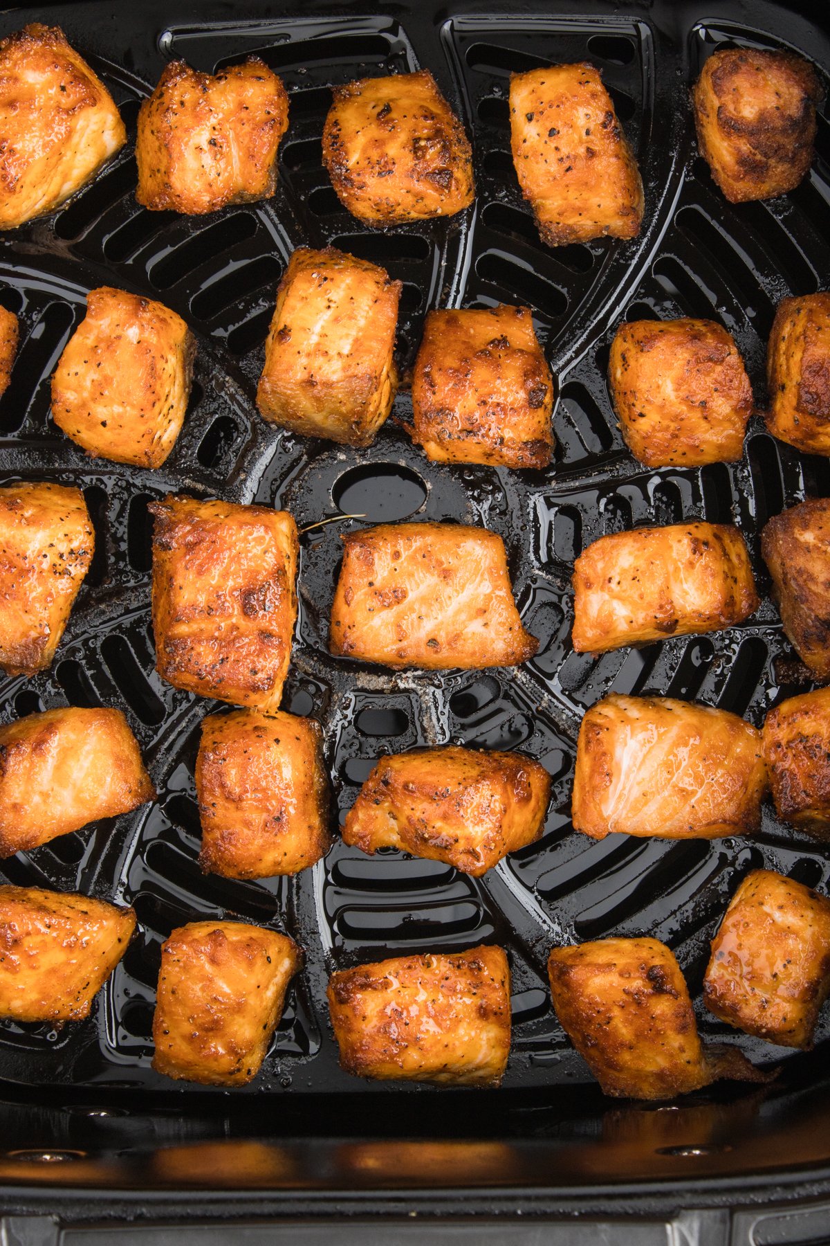Close up of salmon bites in an air fryer basket after they have been cooked.
