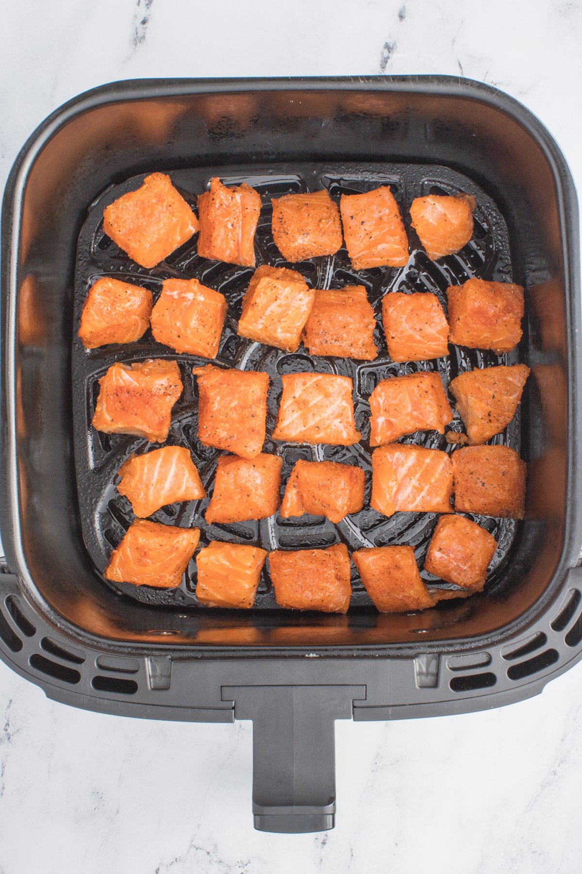 Raw seasoned cubed salmon bites in a single layer in an air fryer basket.