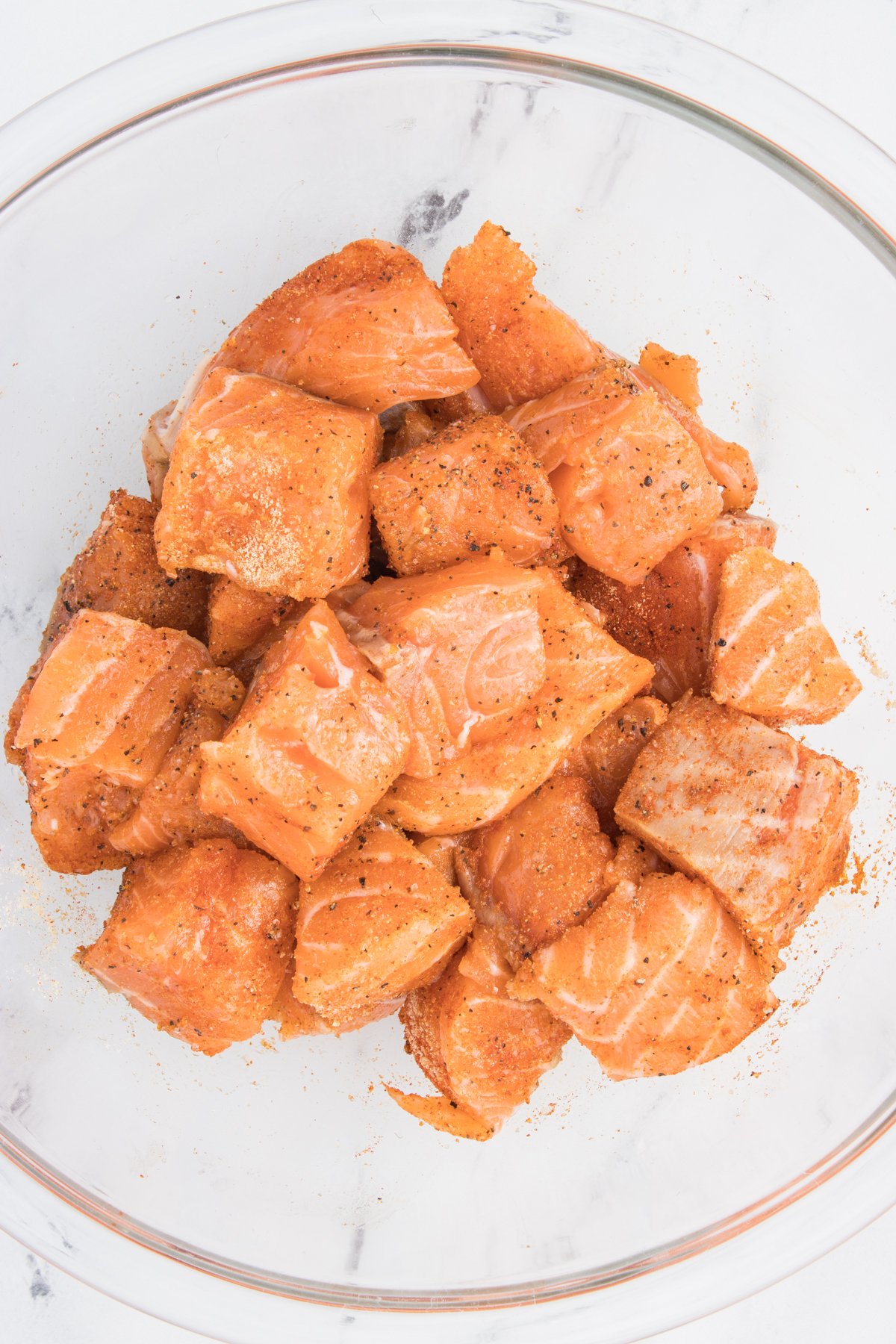 Fresh salmon that has been cut into cubes in a mixing bowl covered in seasoning.