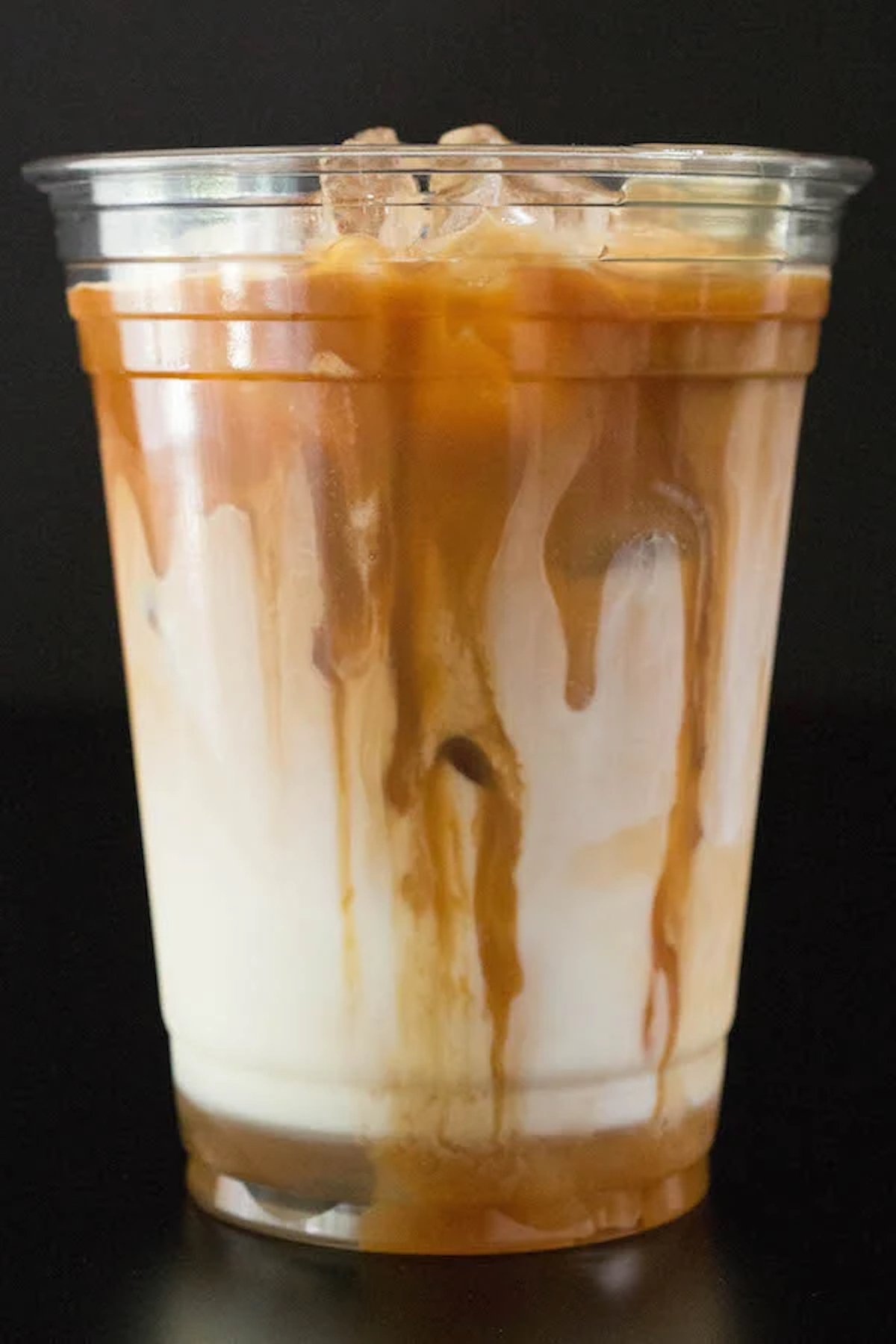 A plastic cup filled with a caramel macchiato that has caramel sauce dripping down the sides.