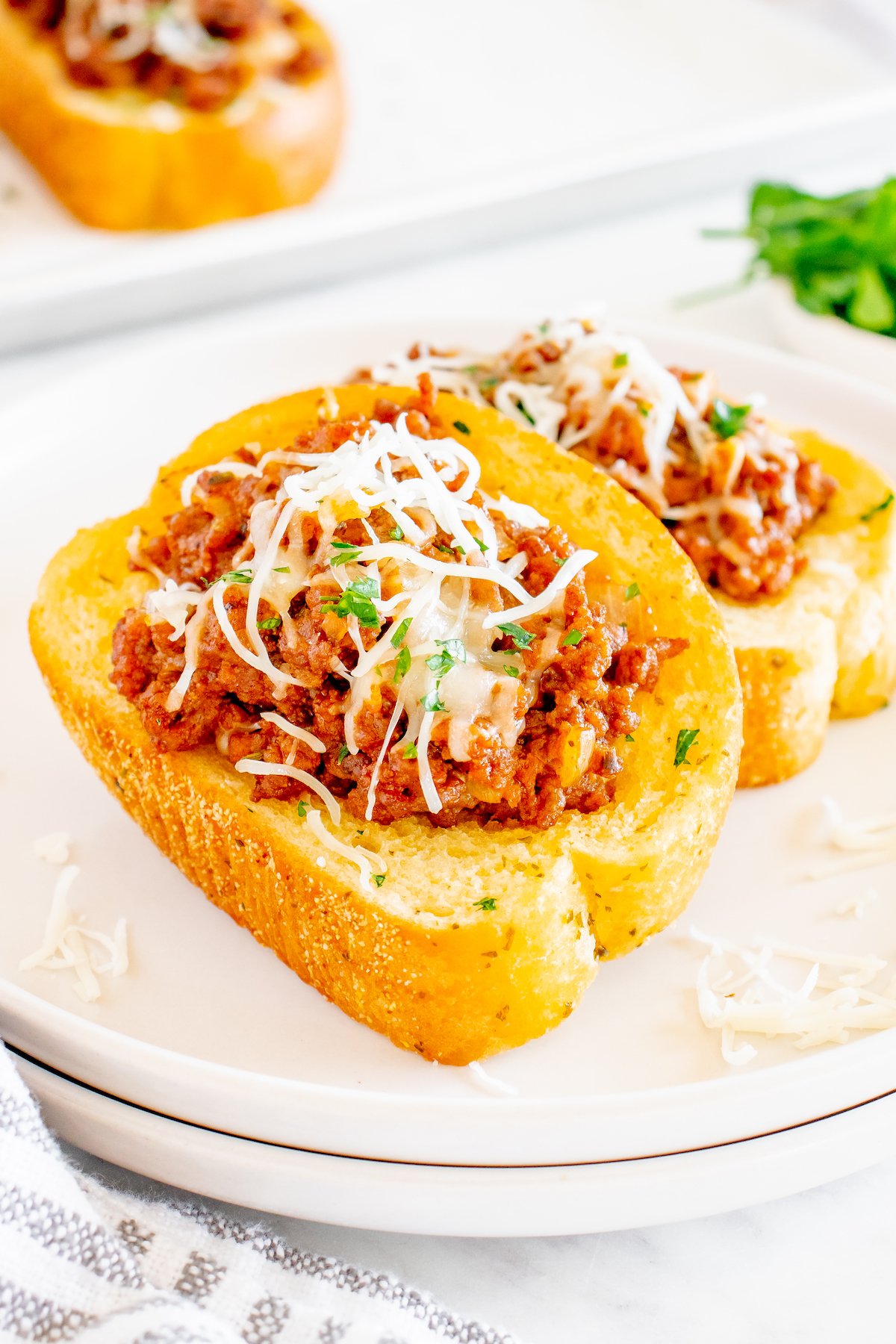 A white serving plate with two slices of Texas Toast that are topped with sloppy Joe mixture and shredded mozzarella cheese.