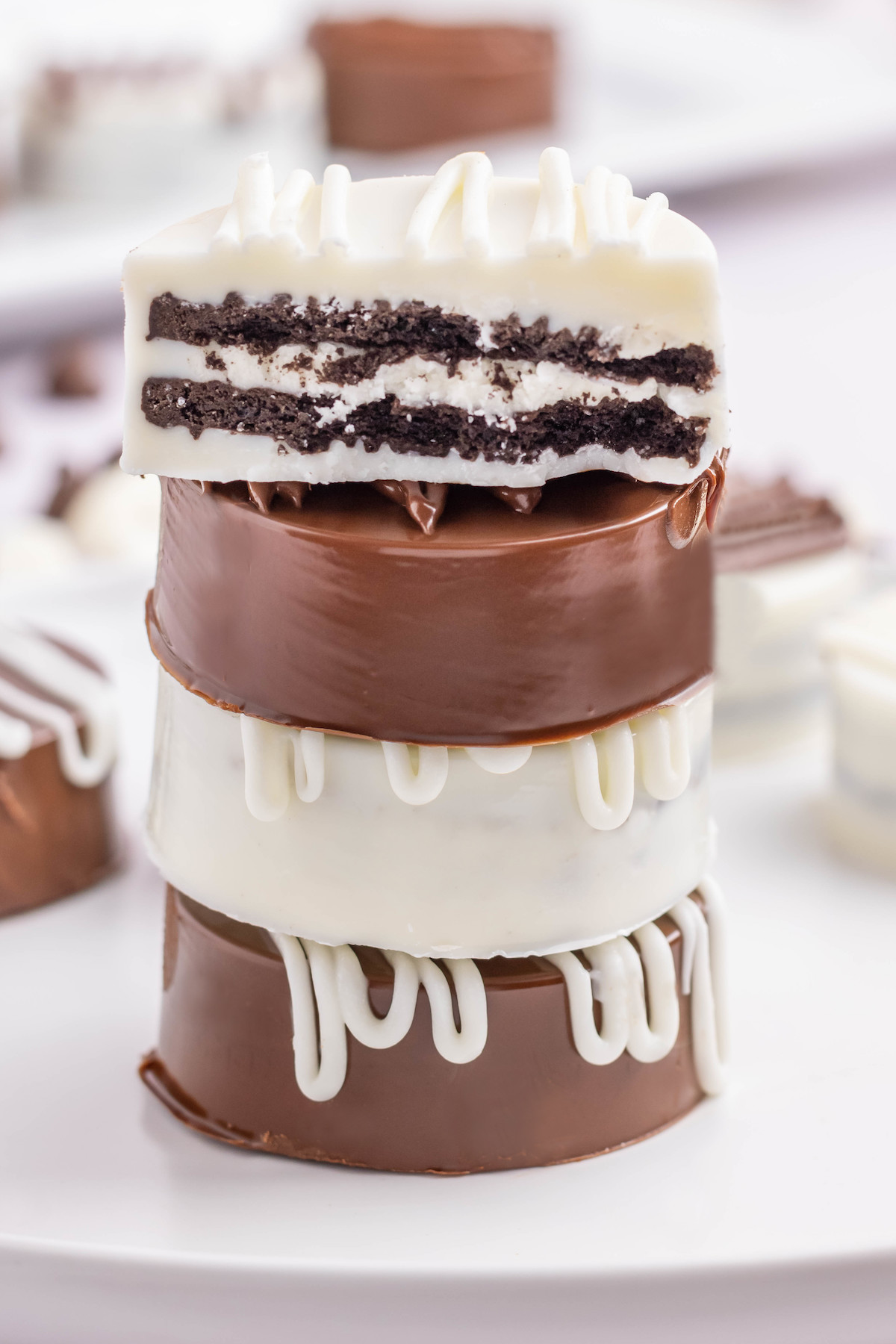 Four white and milk chocolate covered Oreos stacked on top of each other. The top one is cut in half to see the cookie inside.