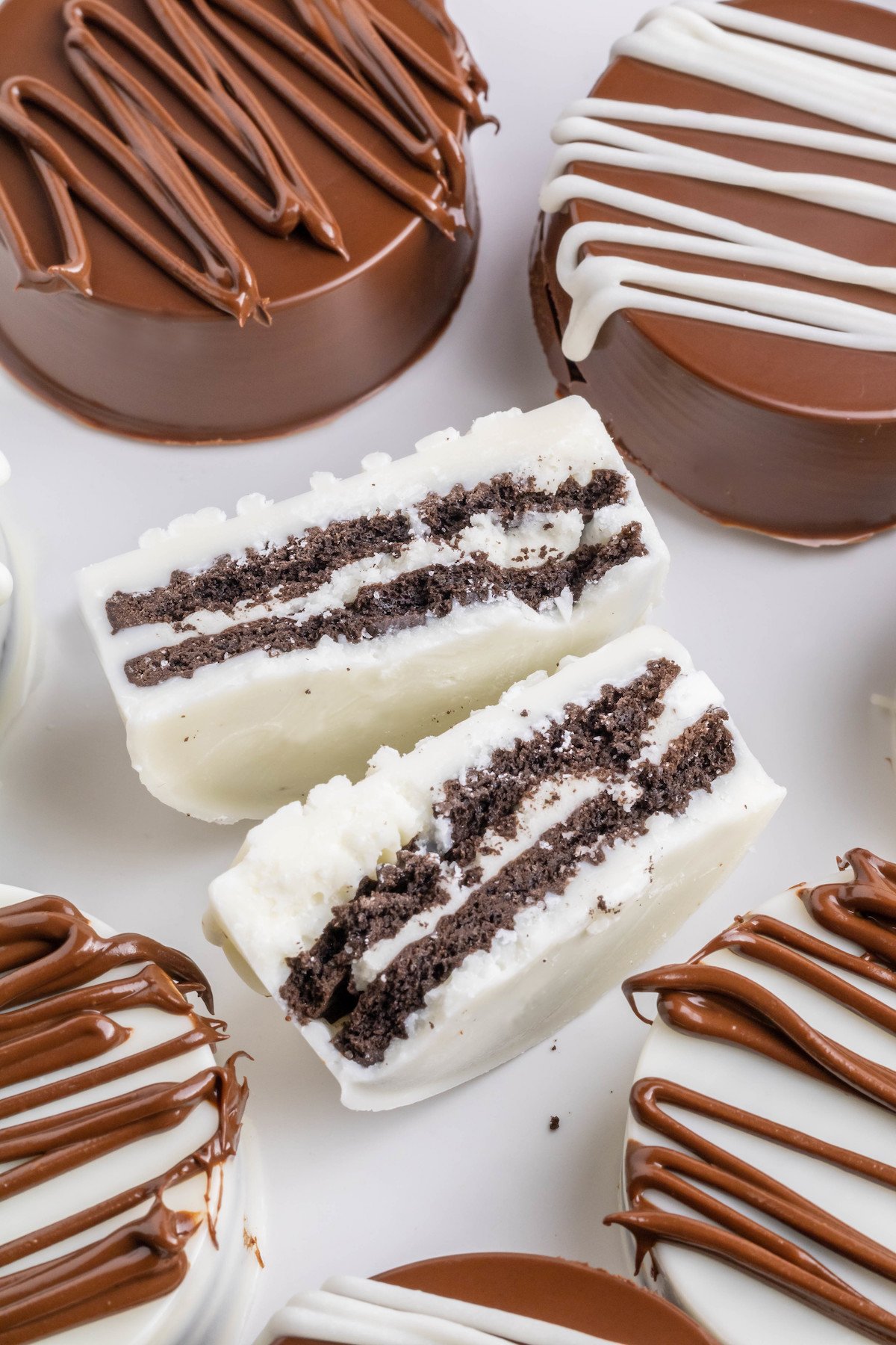 Close up of Oreo cookies that have been completely covered in milk chocolate and white chocolate. The one in the middle is cut in half to show the cookie inside.
