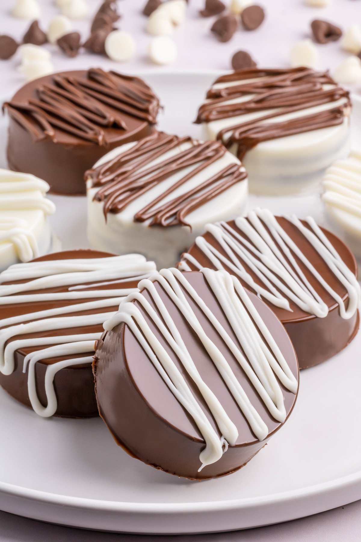 Seven white and milk chocolate covered Oreos on a serving plate. Chocolate chips are out of focus in the background.