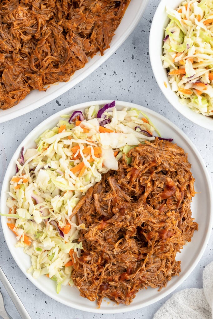 Pulled pork covered in bbq sauce and coleslaw on a dinner plate.