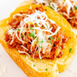 Close up of two pieces of Texas Toast that are topped sloppy joe mixture and shredded white cheese on a white serving plate.