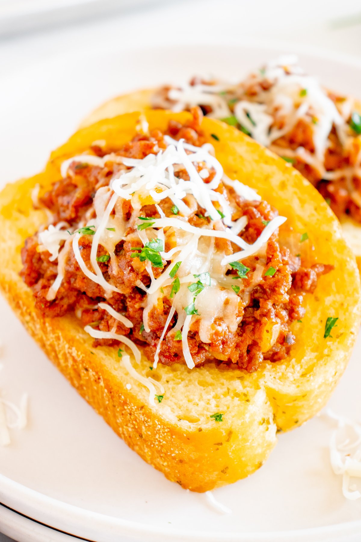 Close up of two pieces of Texas Toast that are topped sloppy joe mixture and shredded white cheese on a white serving plate.