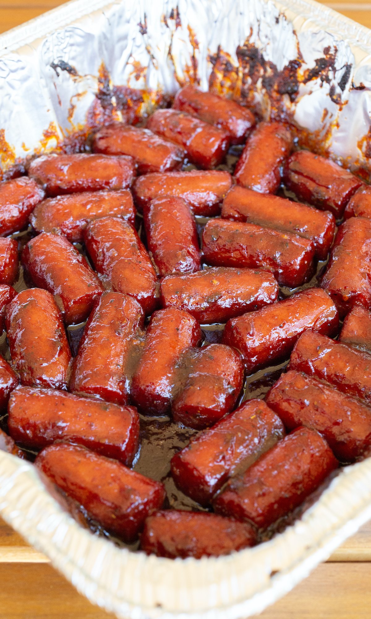A disposable foil pan filled with hot dog burnt ends covered in thick sauce.