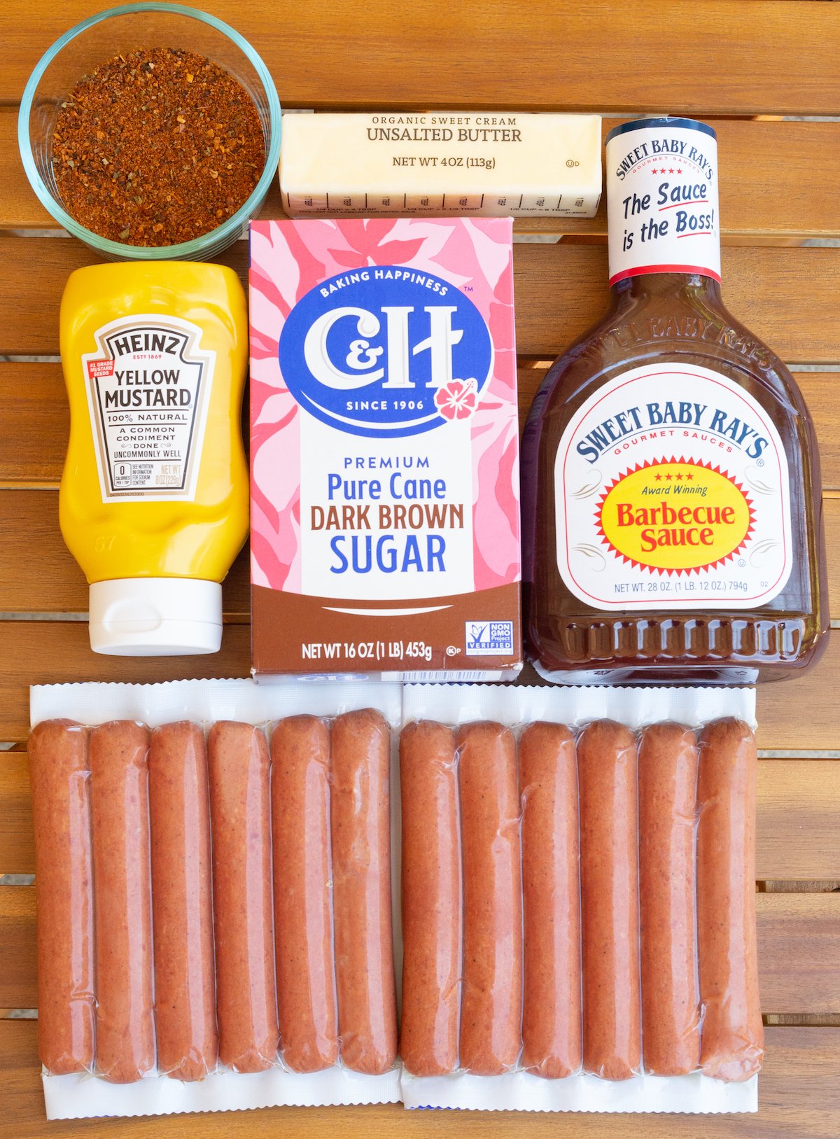 All the ingredients to make hot dog burnt ends laid out on a wooden outdoor table.