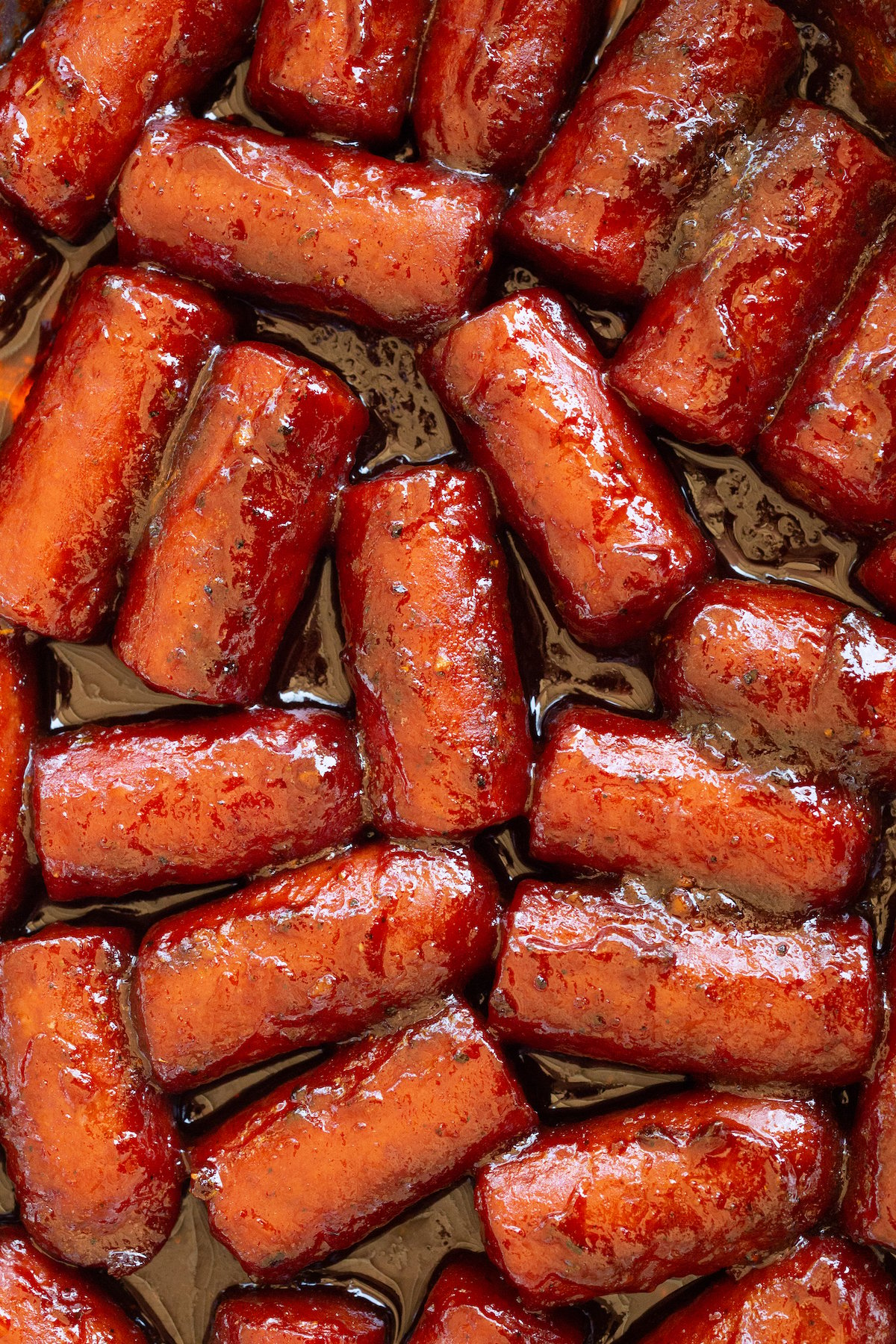 Close up of hot dog wieners cut into thirds and covered in a thick bbq sauce to make burnt ends.