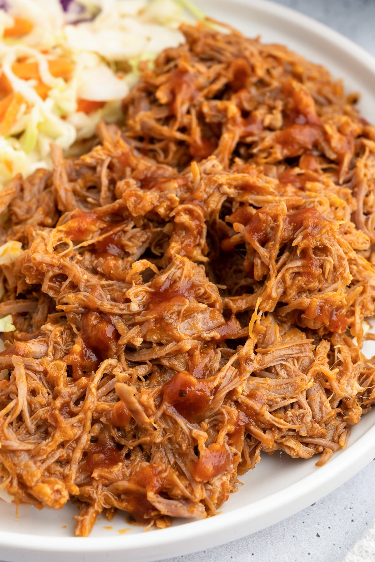 Half of a dinner plate is filled with shredded pulled pork. The other half is out of focus coleslaw.