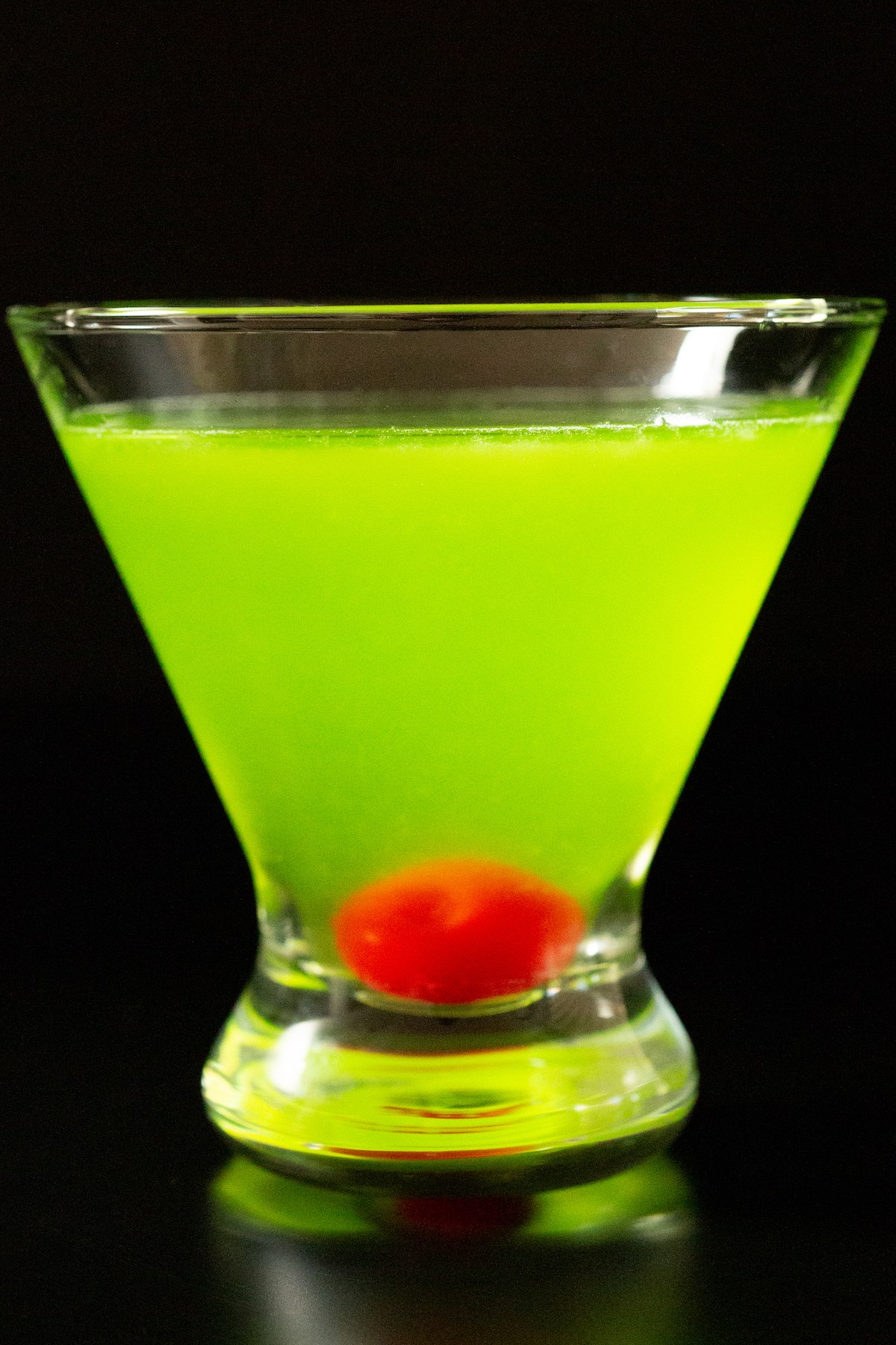 A stemless martini glass with a neon green Japanese Slipper cocktail on a black background.