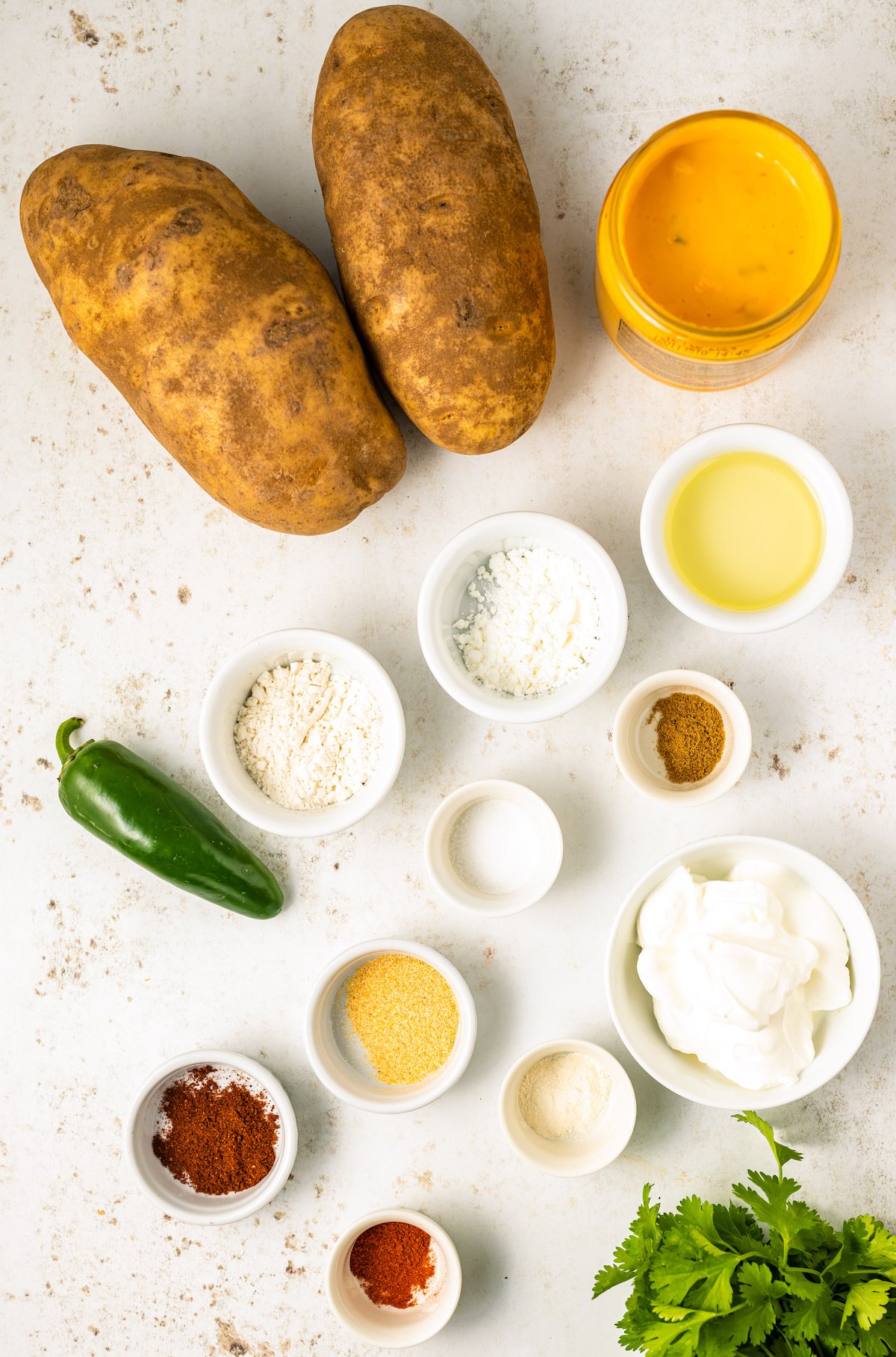 All the ingredients needed to make cheesy fiesta potatoes in prep bowls on a white background.