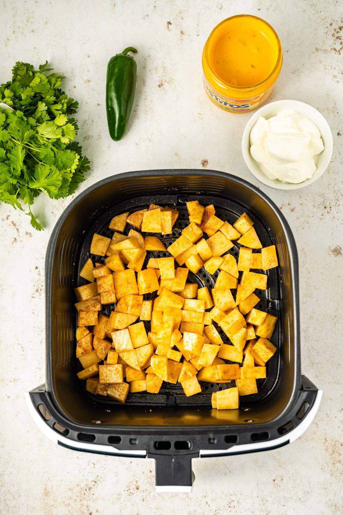 Raw chopped in a seasoned cheesy fiesta potatoes in an air fryer basket before cooking.