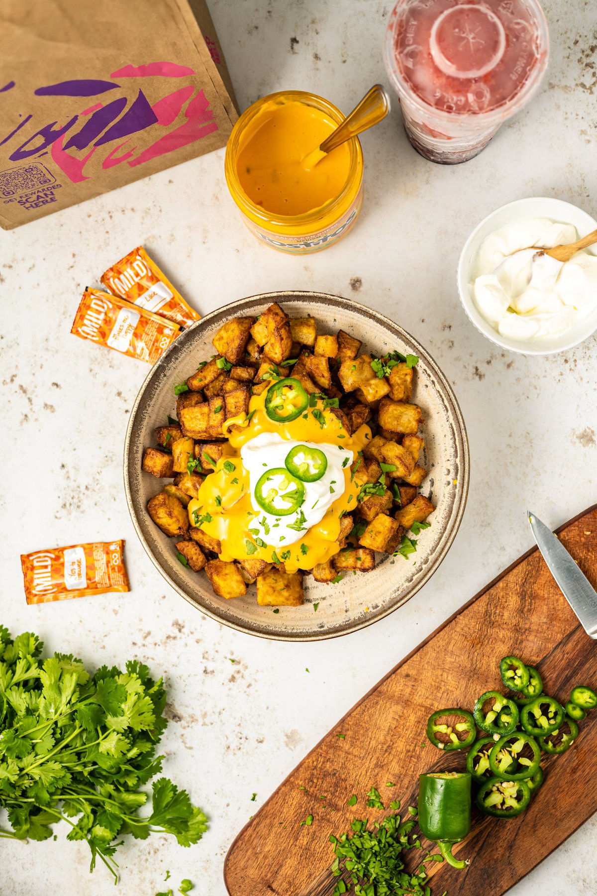 A serving bowl filled with homemade cheesy fiesta potatoes topped with nacho cheese, sour cream, and slice jalapeños.