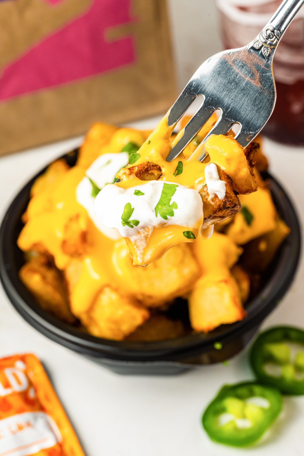 A forkful of homemade cheesy fiesta potatoes is in focus, a bowl with more potatoes is out of focus in the background.