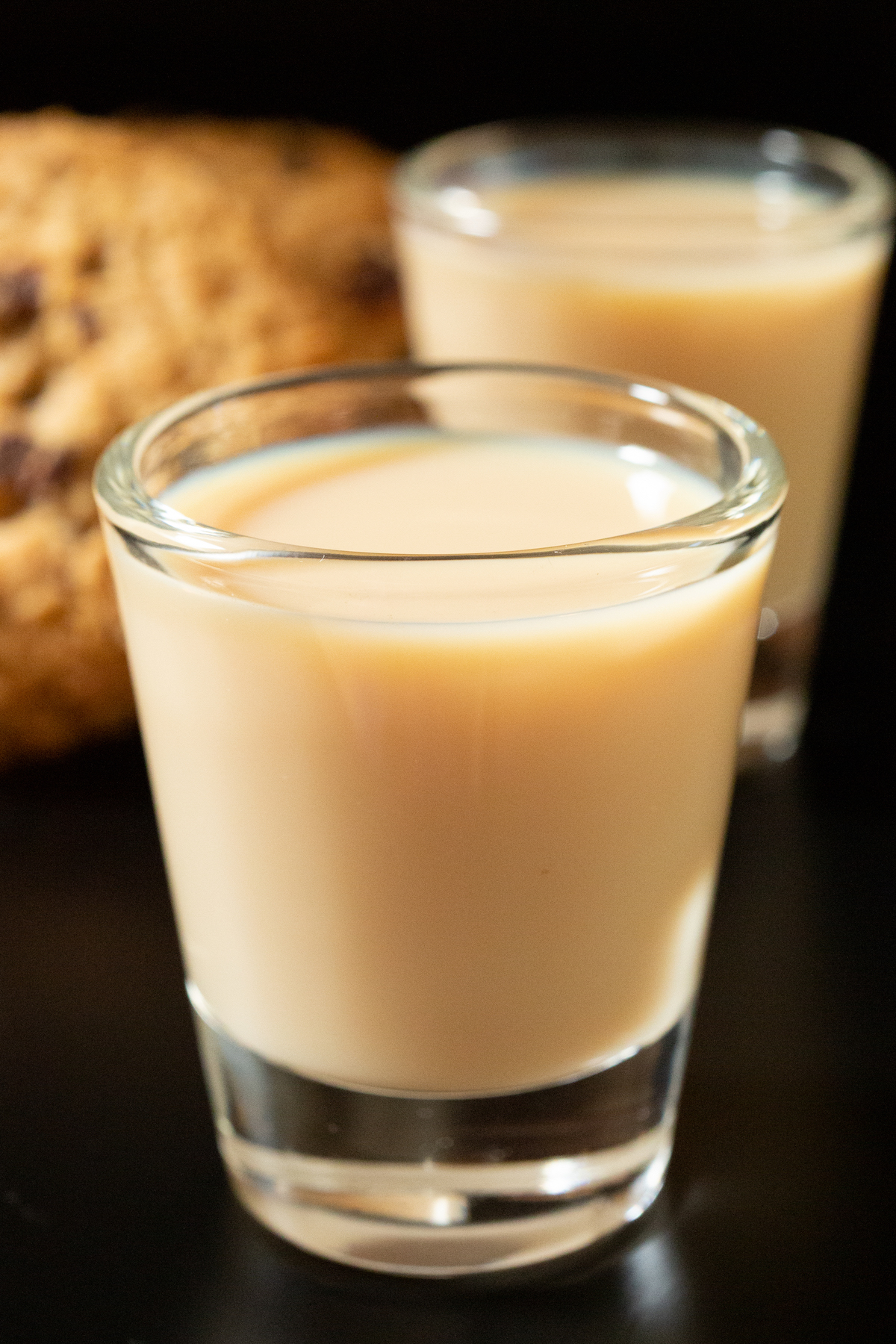Two shot glasses filled with creamy brown oatmeal cookie shots. One is in focus and the other in the background out of focus.