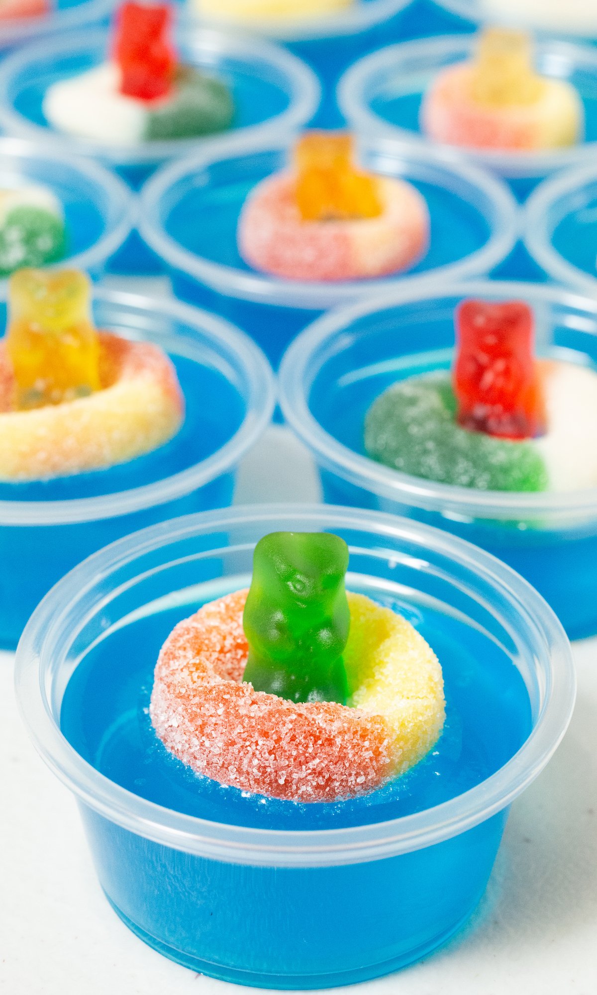 9 2oz plastic containers filled with bright blue jello topped with a candy gummy bear and gummy ring.