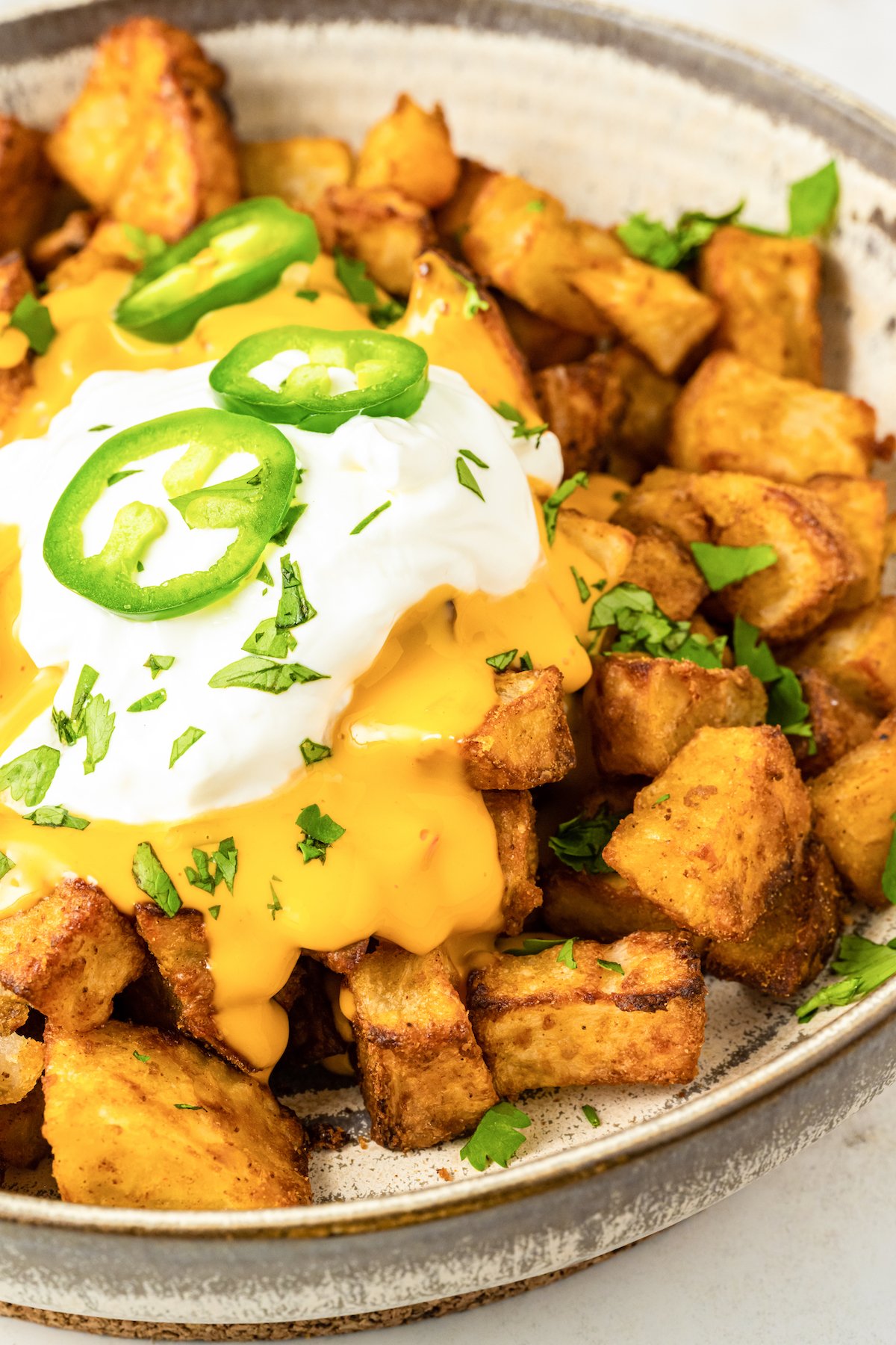 Close up of chopped seasoned crispy cheesy fiesta potatoes covered in nacho cheese, sour cream, chives, and jalapeno slices.