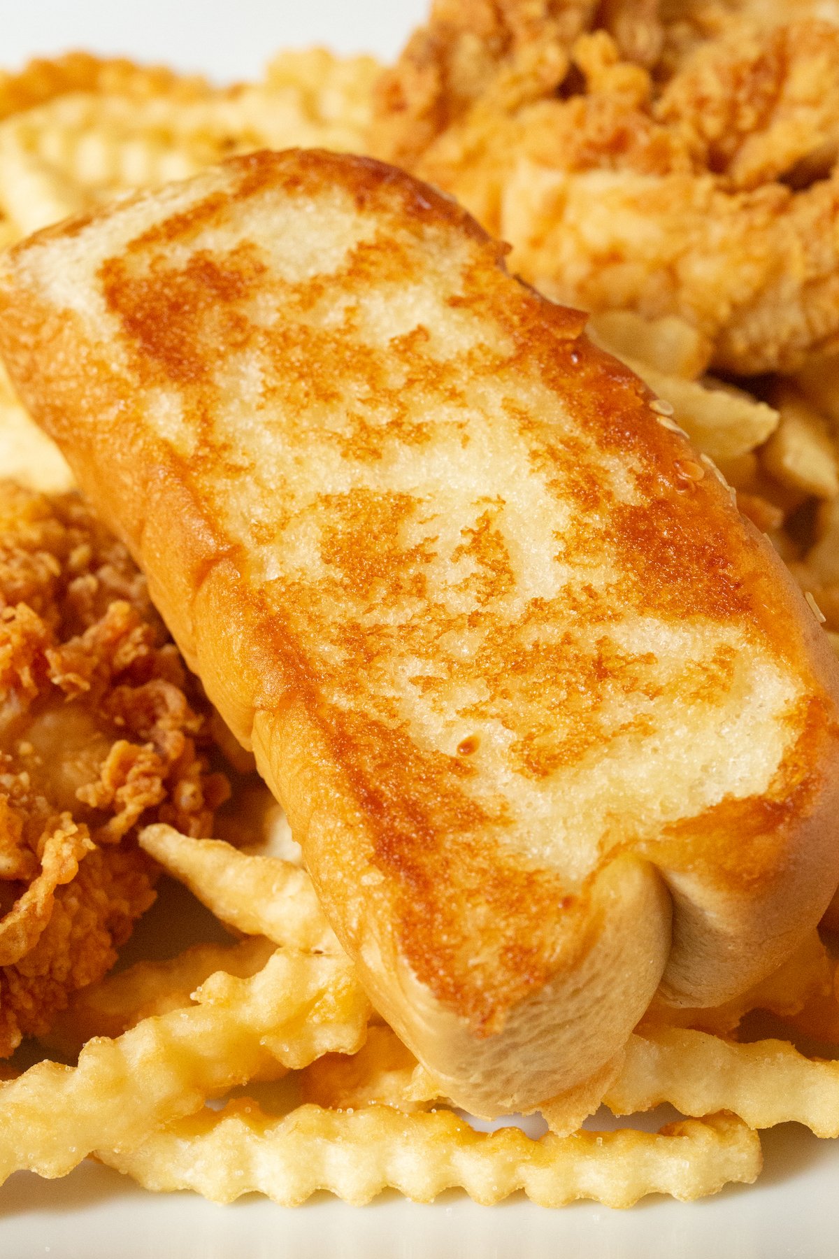 A slice of homemade Raising Canes garlic bread on top of crinkly fries and chicken tenders.