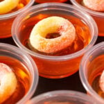 Several rows of peach jello shots topped with peach gummy rings in rows on a black background.