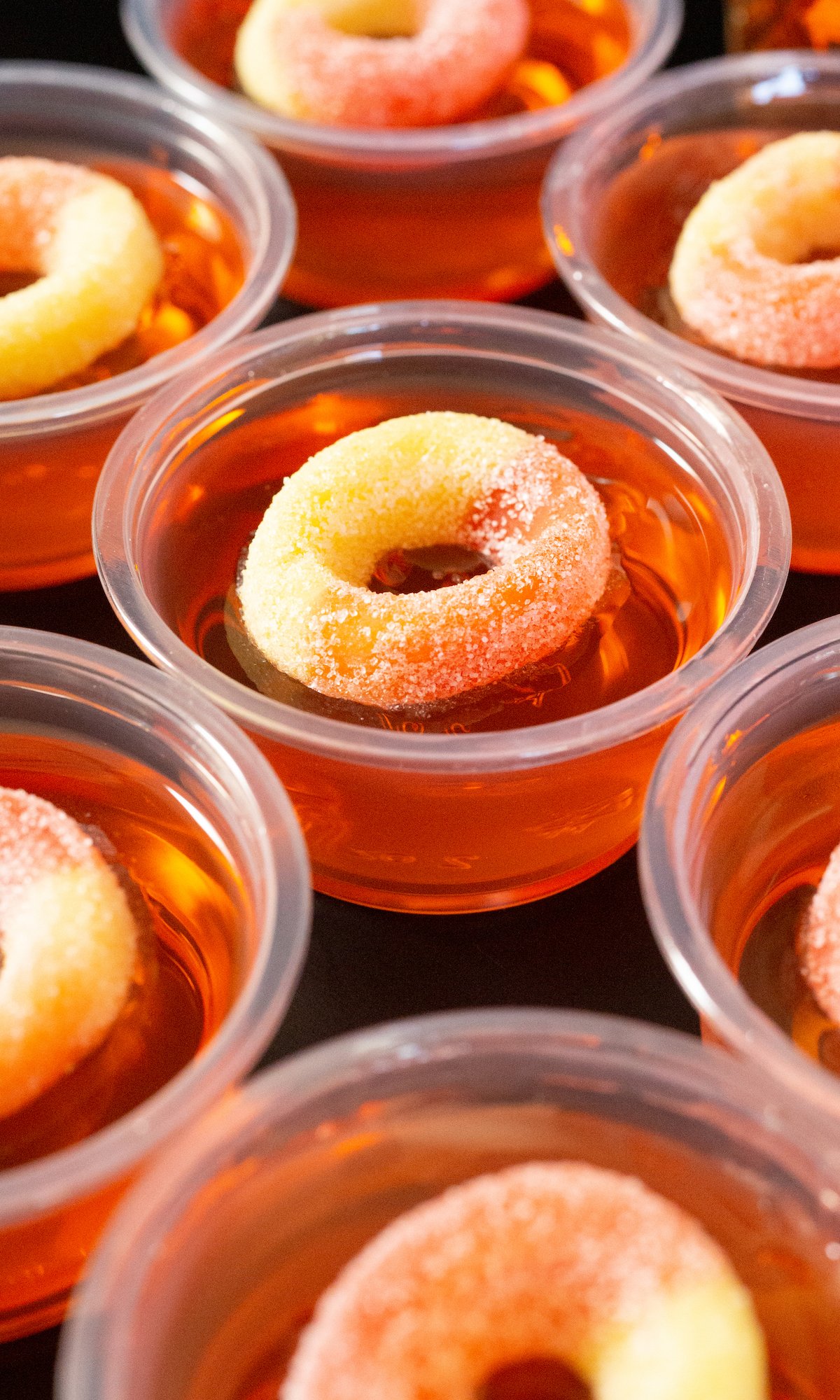 Several rows of peach jello shots topped with peach gummy rings in rows on a black background.