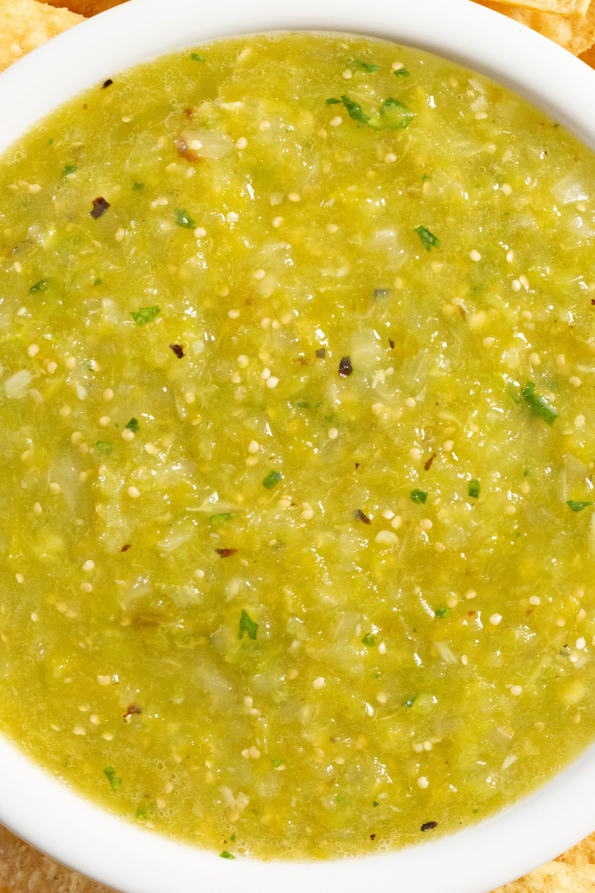 Close up of a green hatch chile salsa in a white serving bowl.
