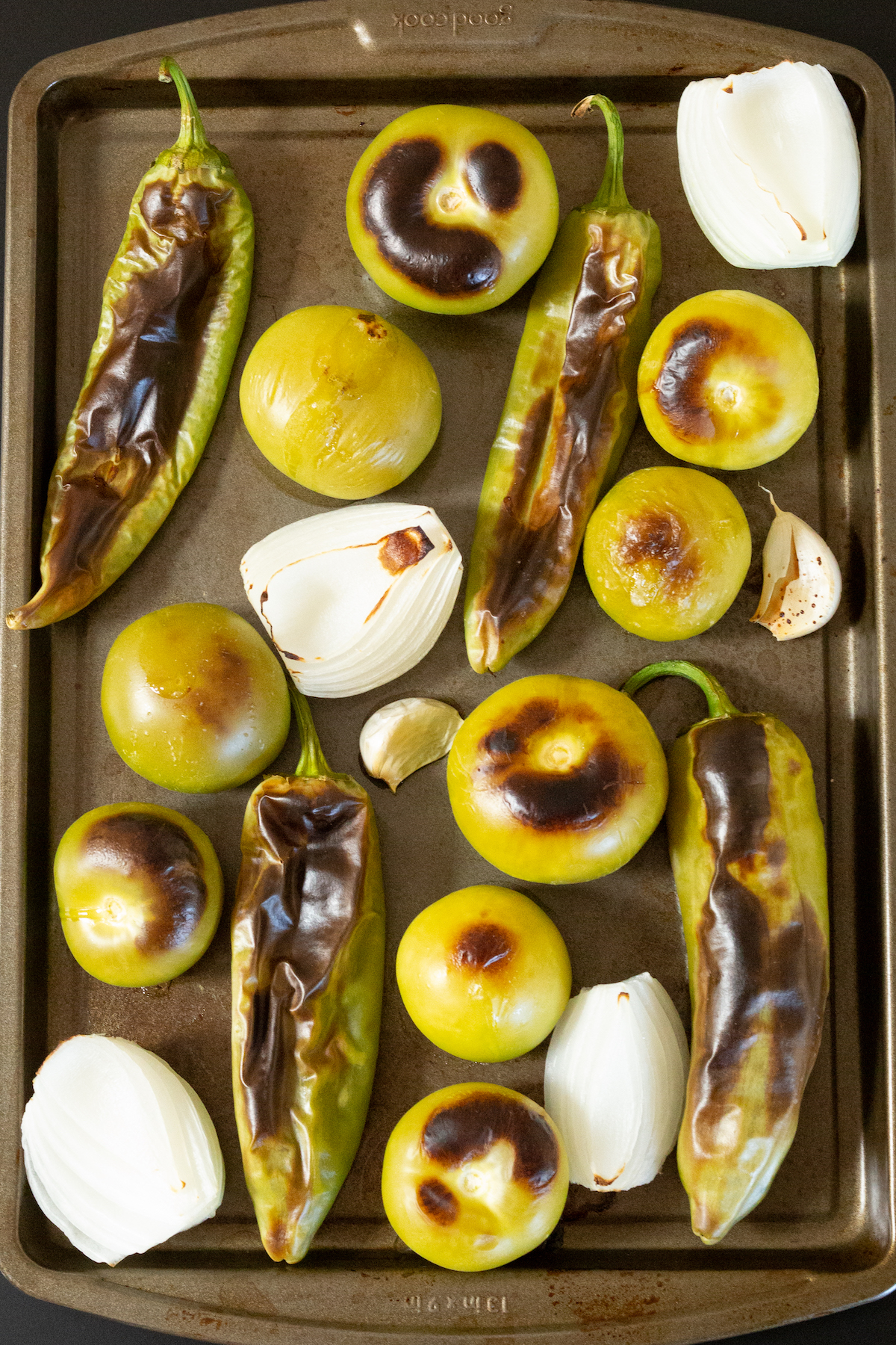 A baking sheet filled with roasted hatch chiles, tomatillos, white onion, and garlic.