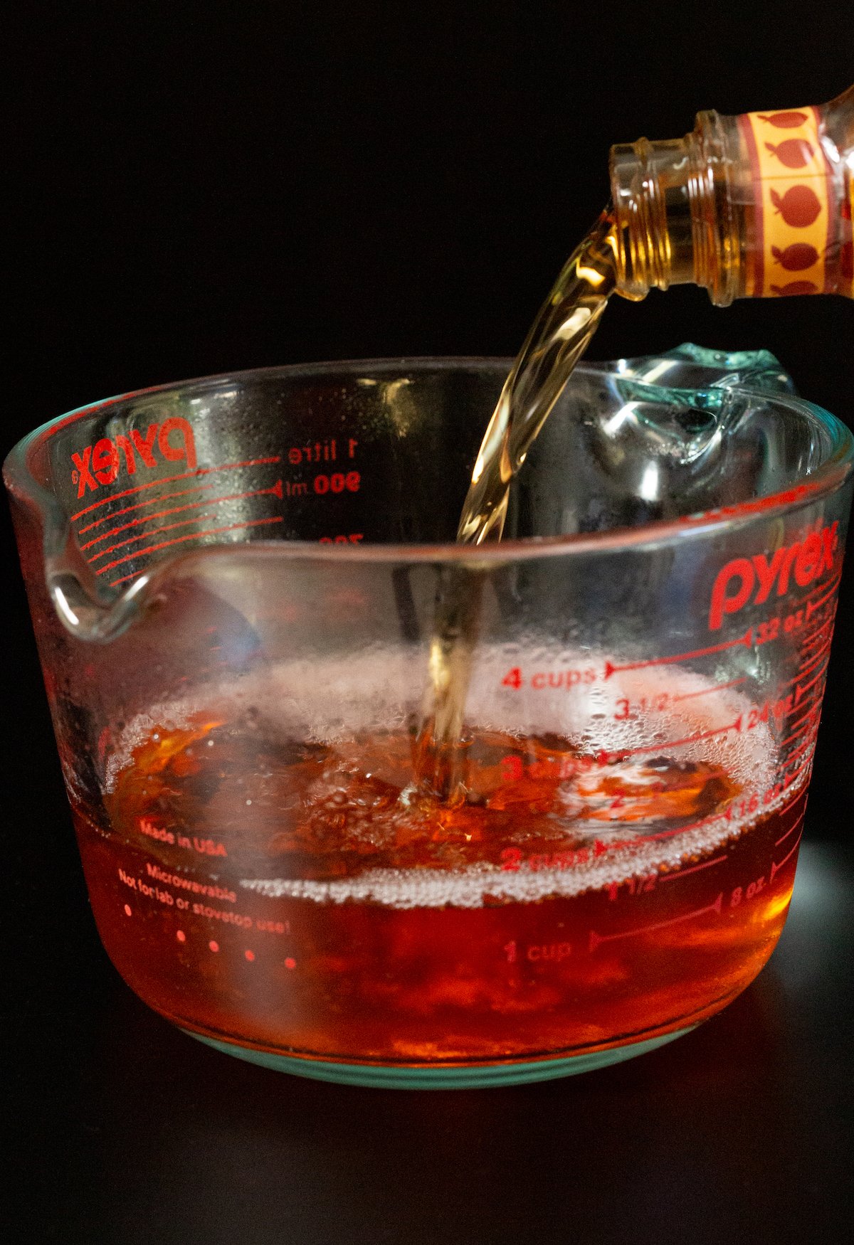 A large pyrex cup with liquid peach gelatin being filled with Crown Peach whisky.