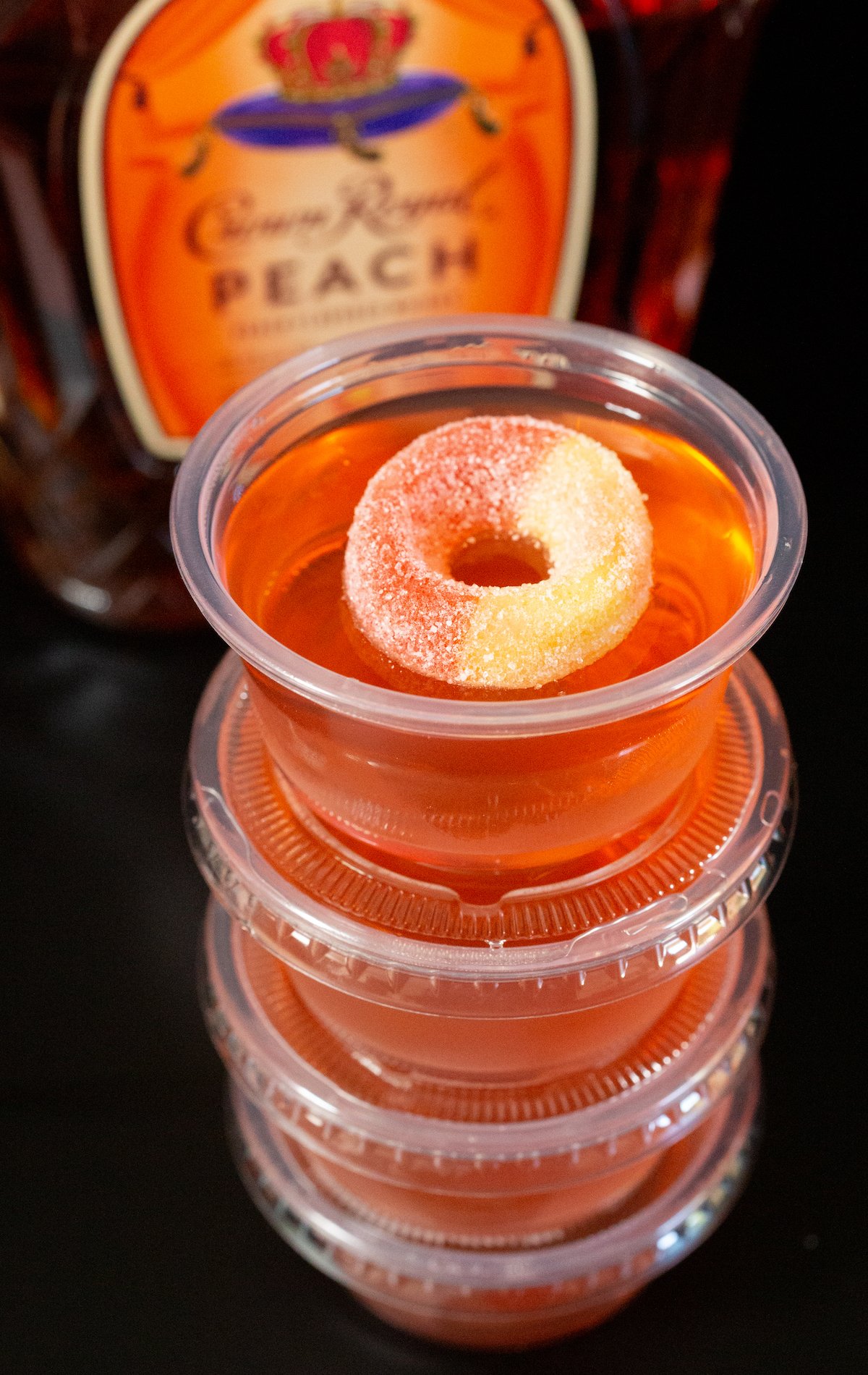4 2 oz plastic containers filled with peach jello shots stacked in front of a Peach Crown bottle.