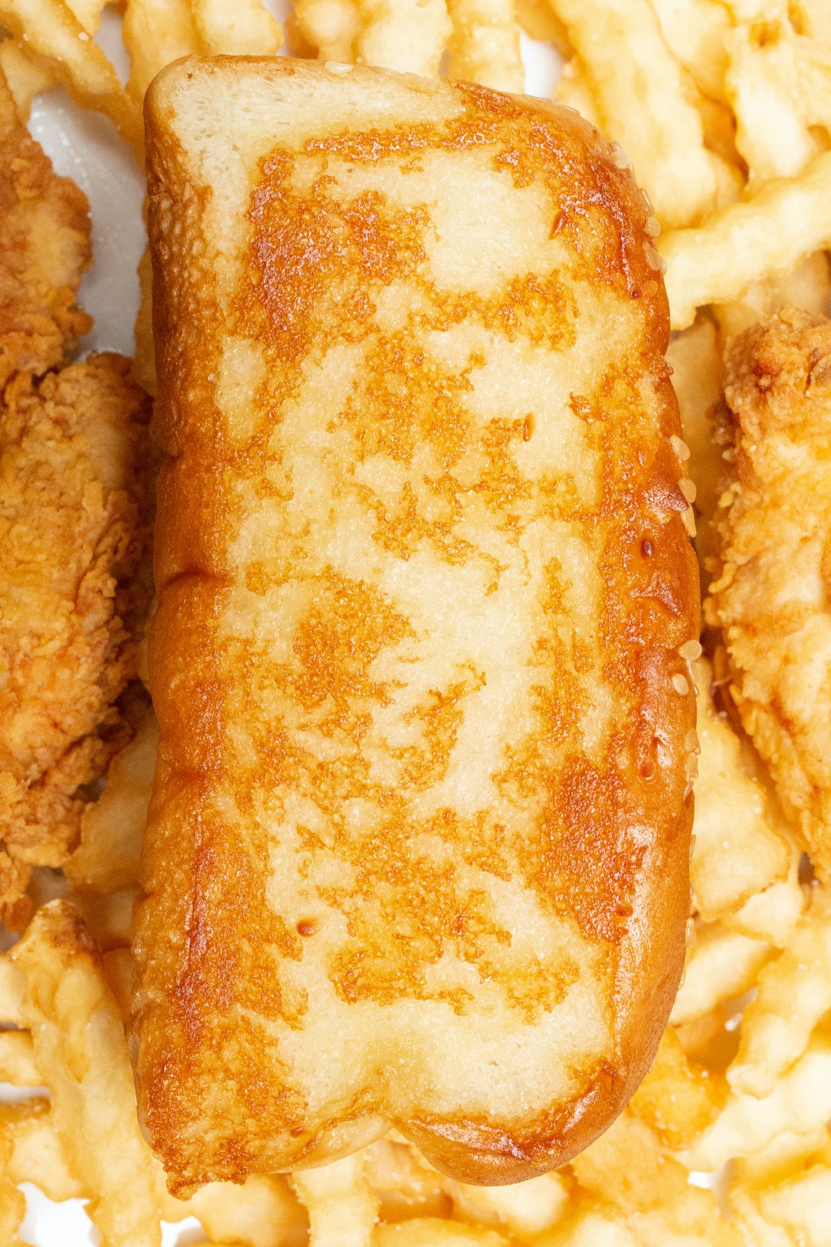 A slice of homemade Raising Canes bread on top of crinkly fries next to chicken tenders.