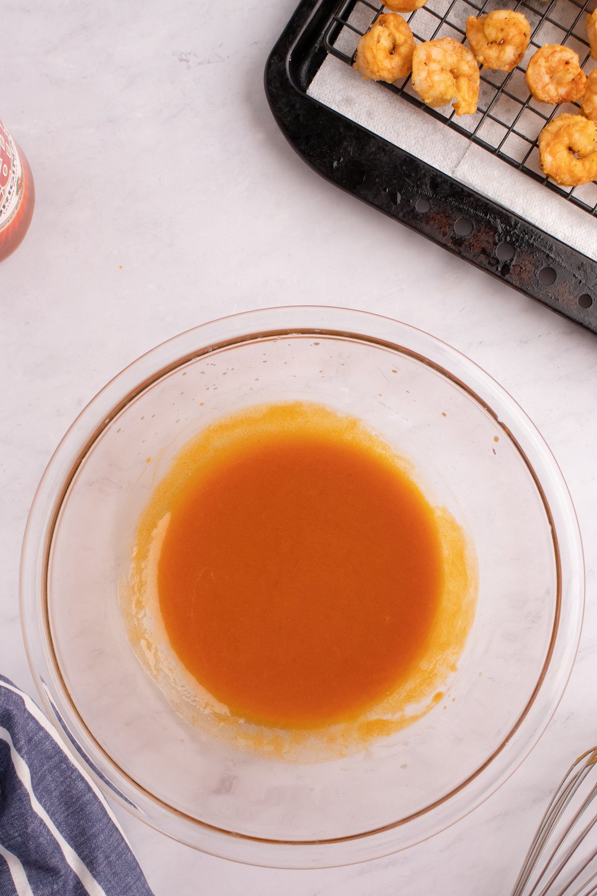 A glass mixing bowl filled with hot sauce and melted butter.