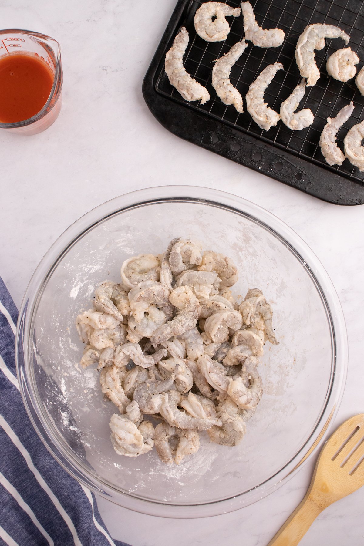 Raw shrimp tossed with cornstarch and spices in a mixing bowl.