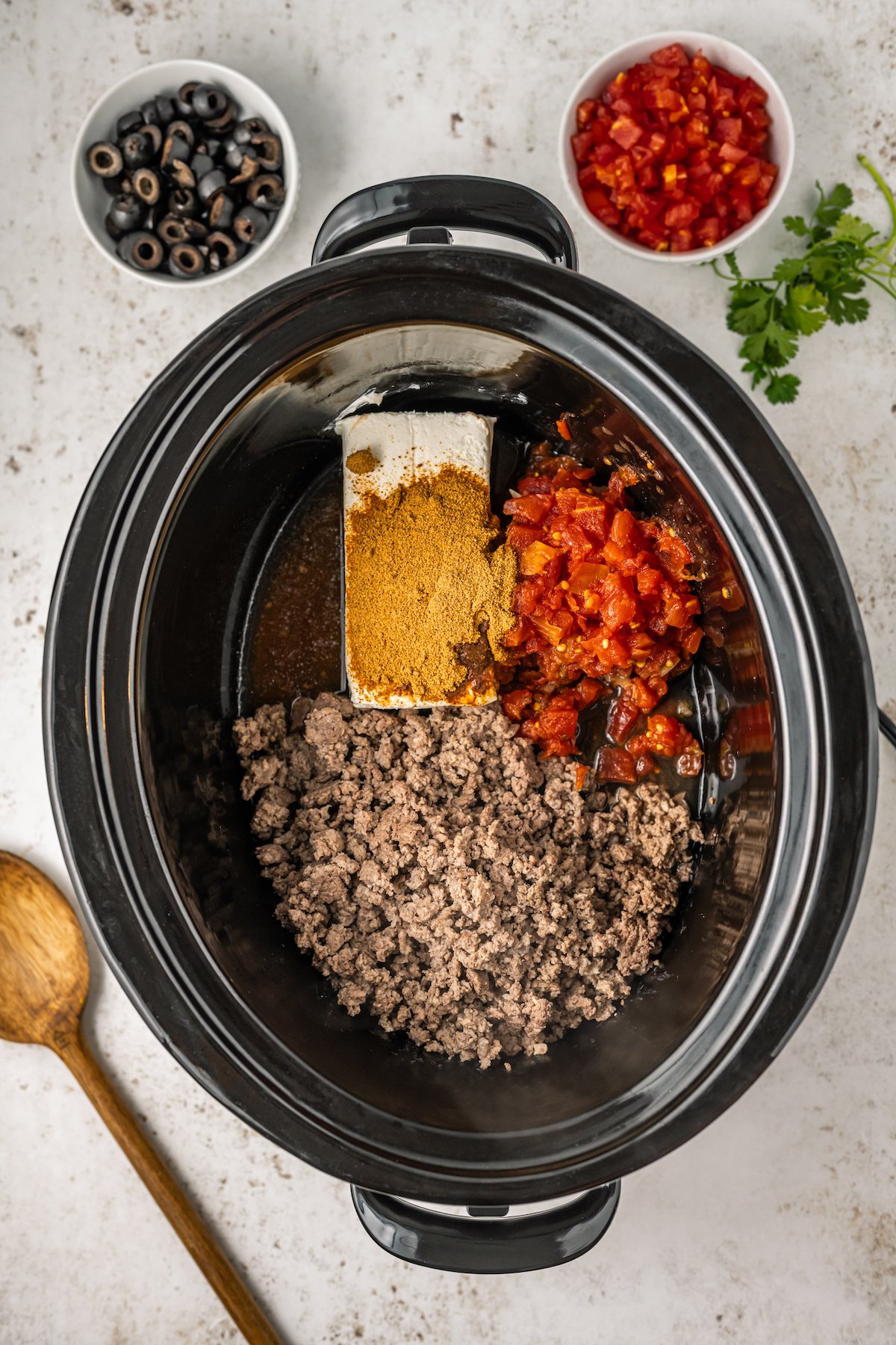 A crock pot filled with browned ground beef, Rotel, and taco spices.