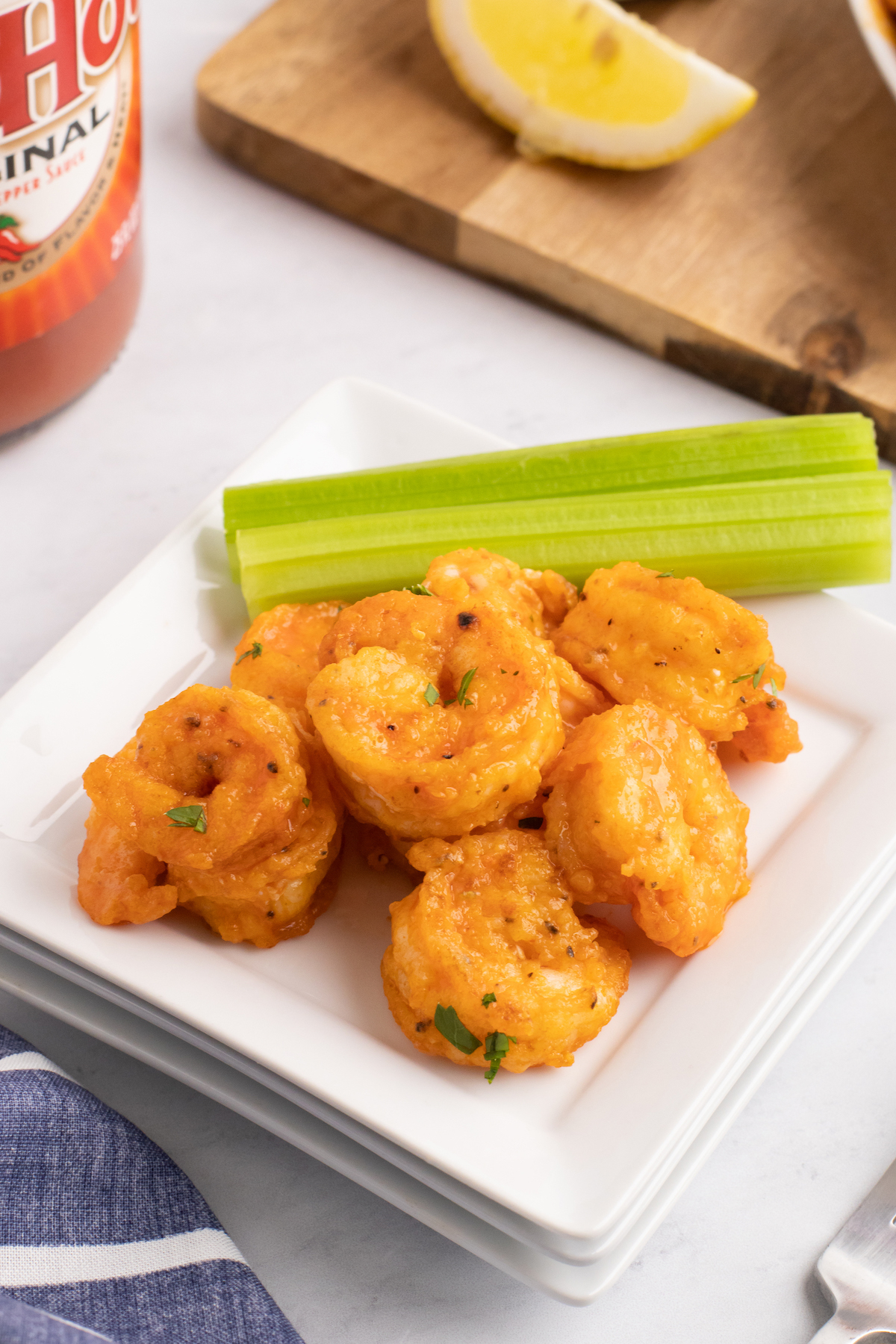 A small serving dish with six buffalo shrimp and a celery stick.