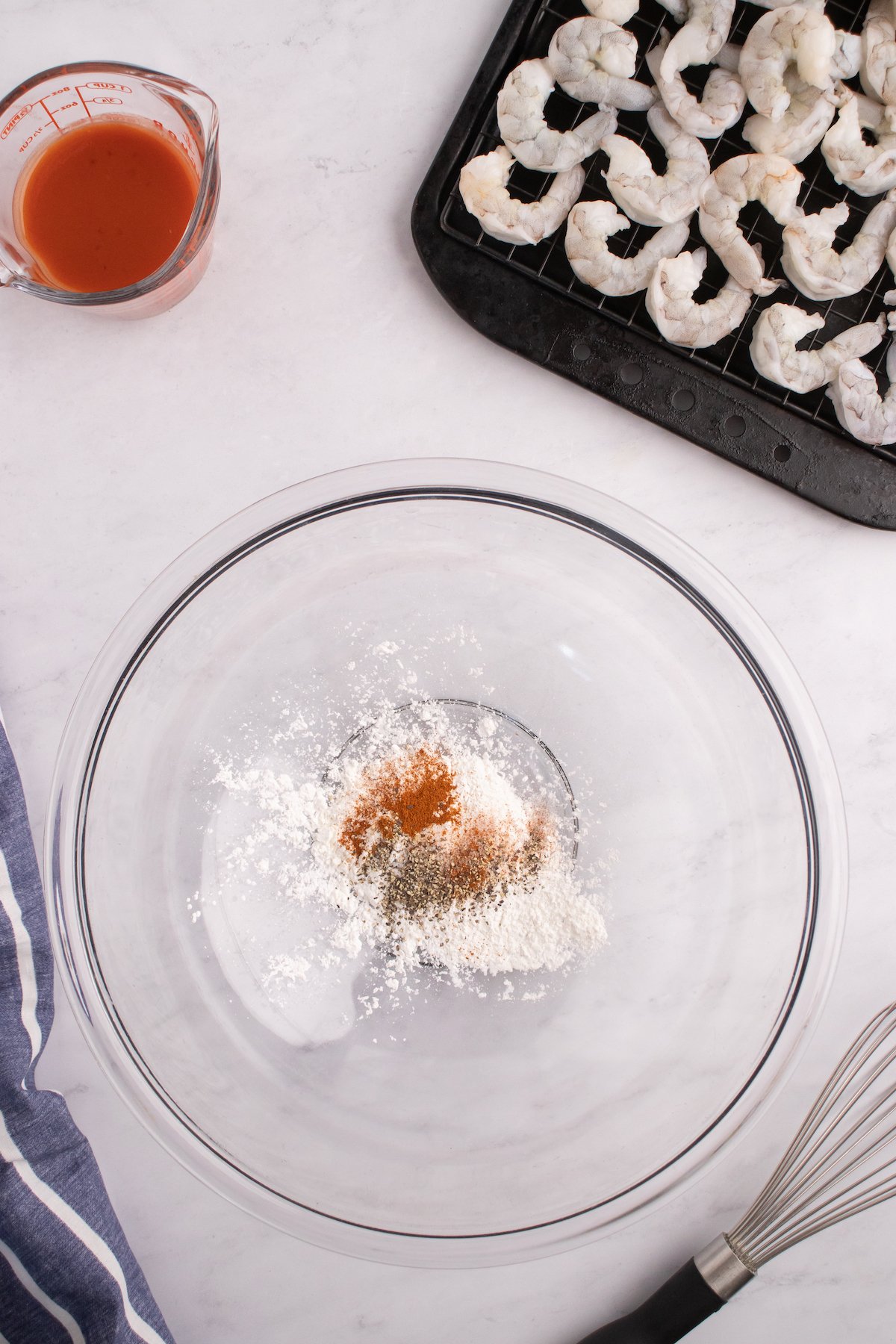 A mixing bowl filled with cornstarch and spices. A pan of raw shrimp is next to it.