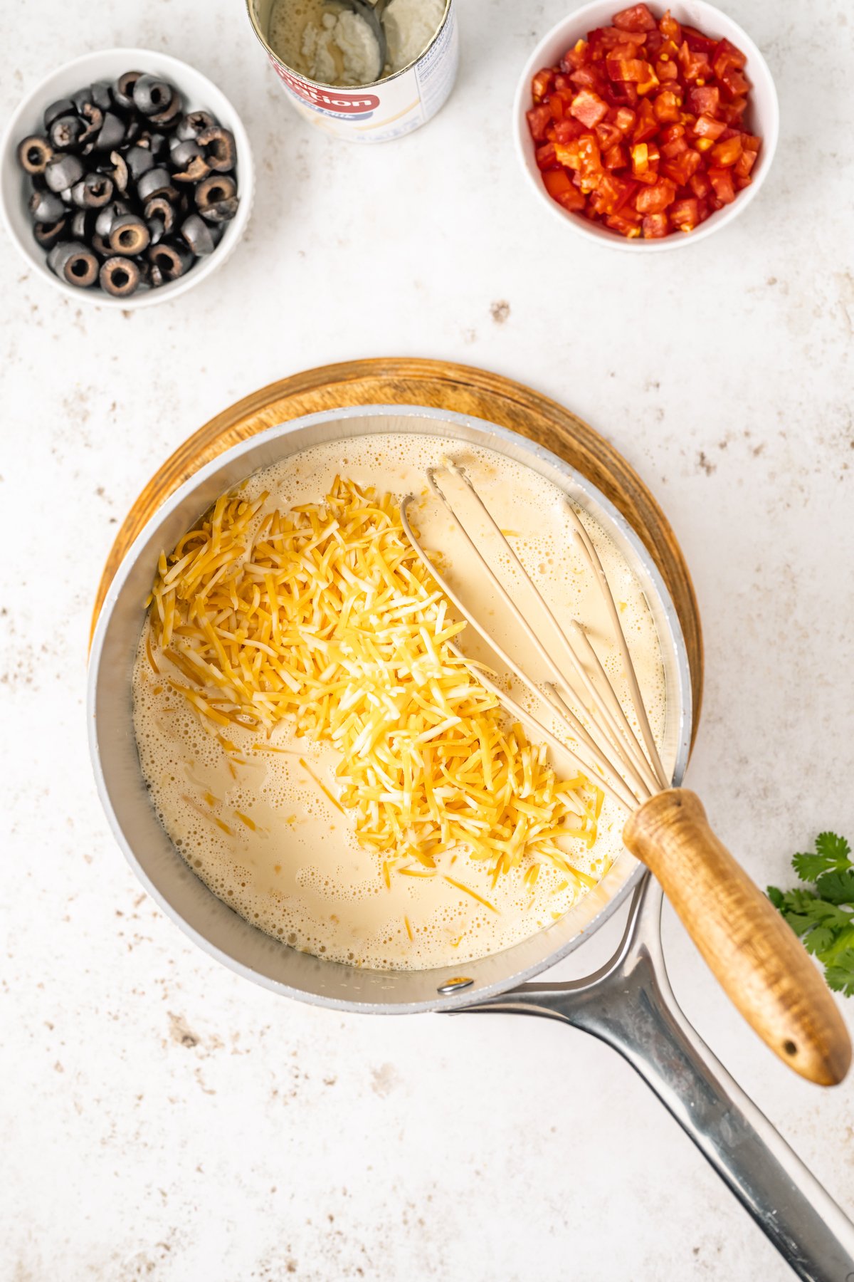 A small sauce pan with condensed milk and shredded cheese.