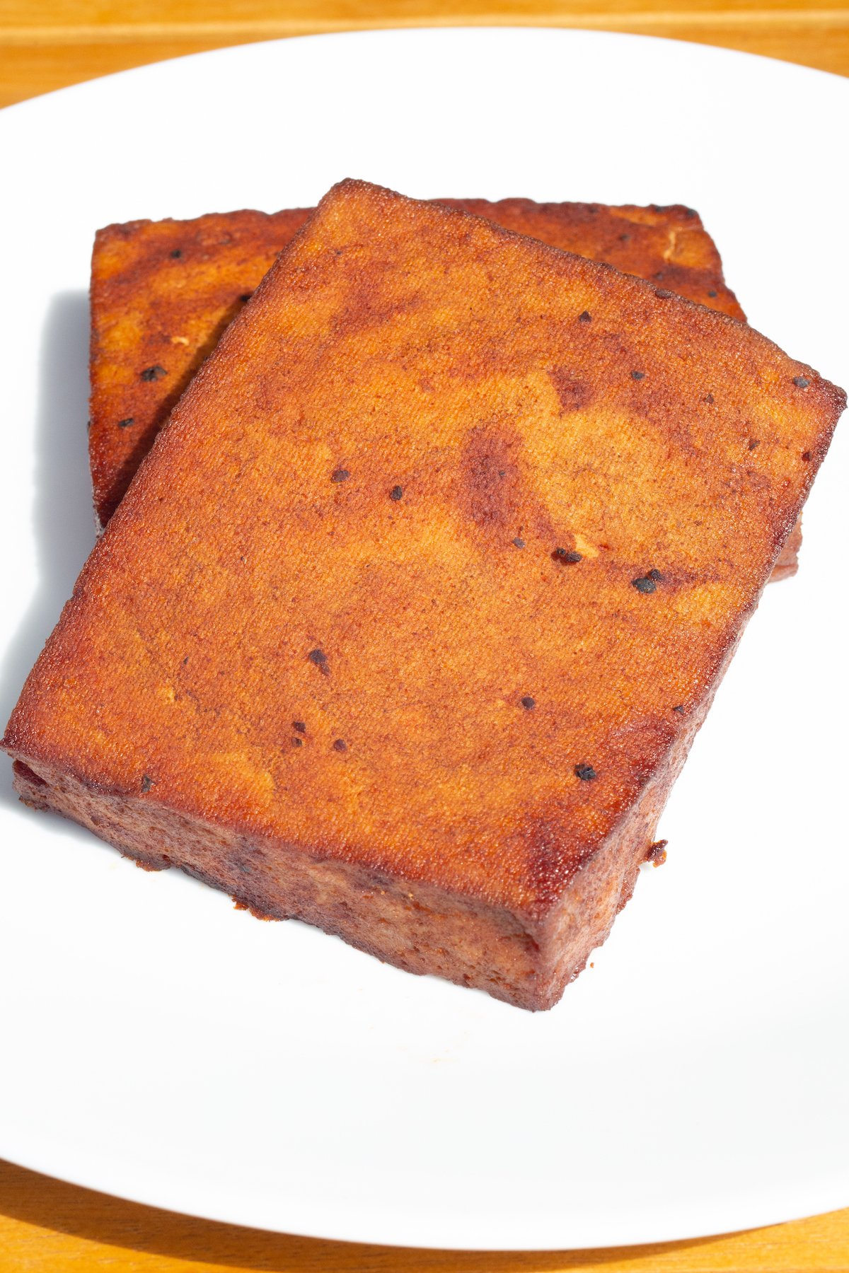 Two blocks of smoked tofu that have been turned a deep red by the barbecue sauce sit on a white serving plate.