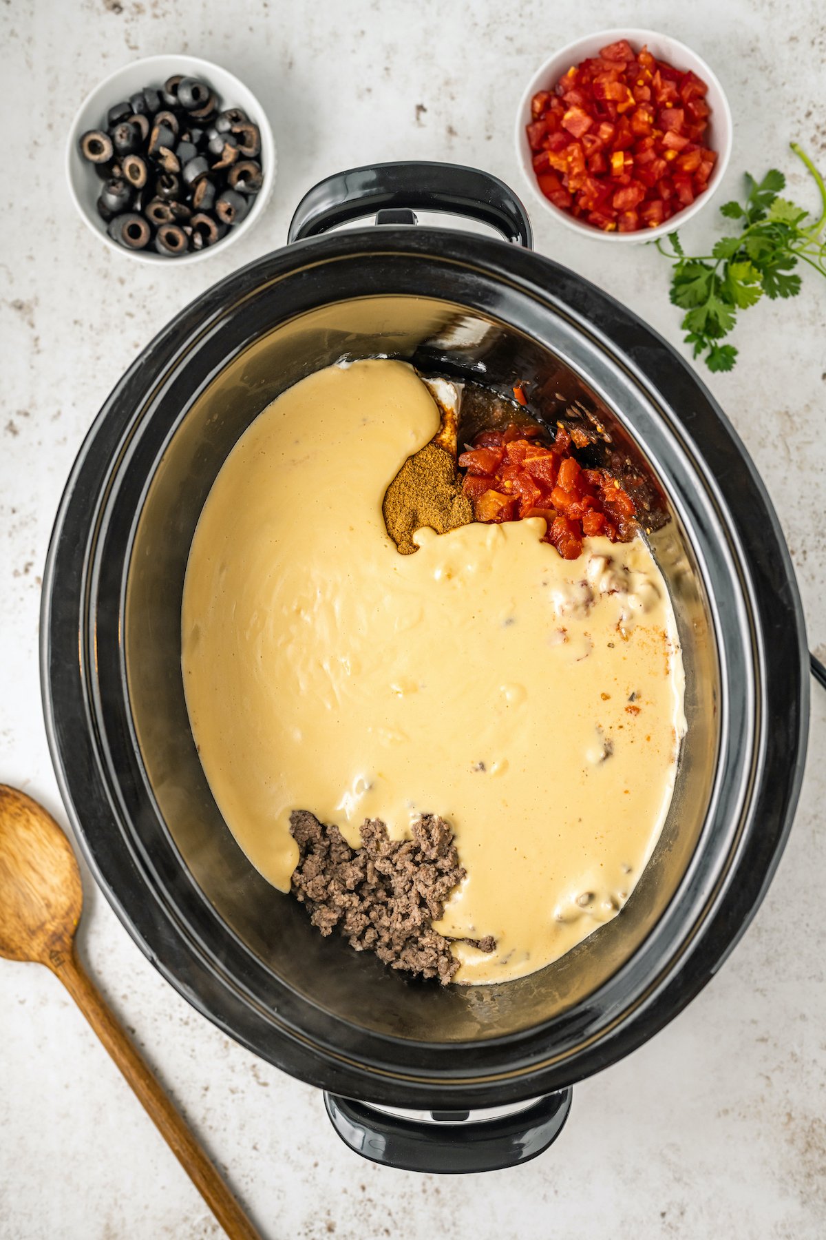 A crock pot filled with browned ground beef, cream cheese, Rotel, and spices is covered in homemade queso.