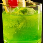 A lowball glass is filled with a neon green Midori Sour cocktail that is garnished with a lemon wheel and maraschino cherry.