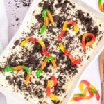 A large baking dish is filled with an Oreo dirt cake that's topped with crumbled cookies and colorful gummy worms.