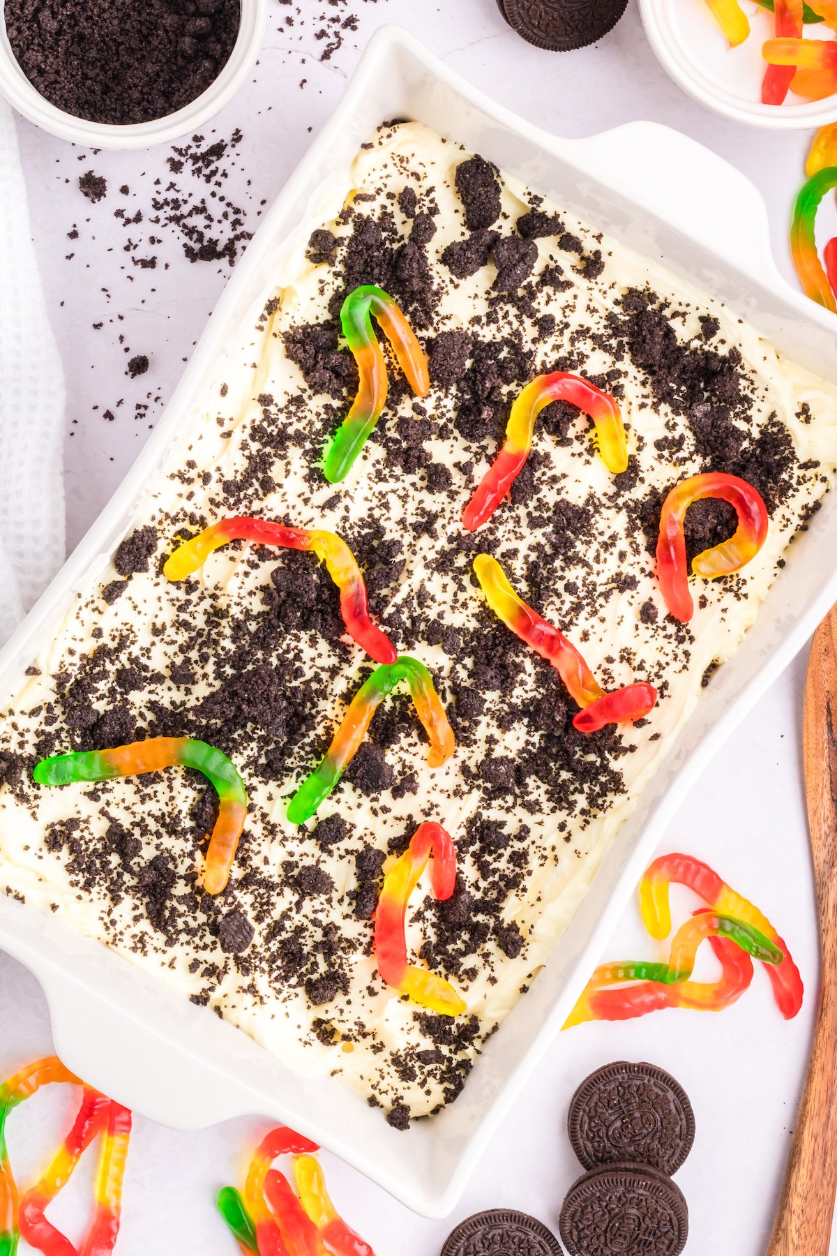 A large baking dish is filled with an Oreo dirt cake that's topped with crumbled cookies and colorful gummy worms.