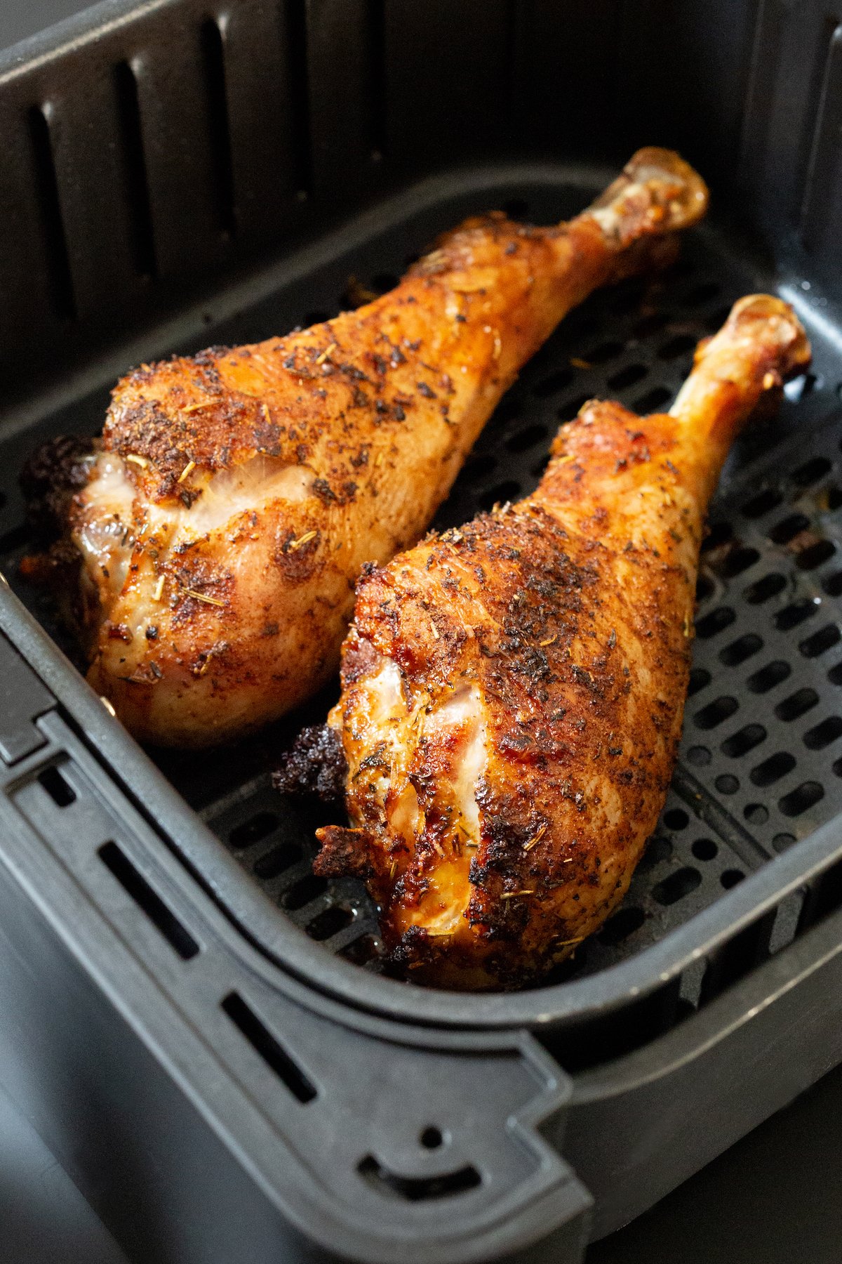 A black air fryer basket with two cooked turkey legs.